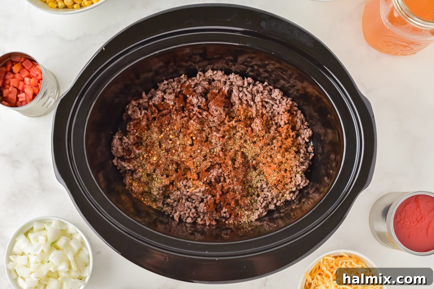 Seasonings sprinkled on top of browned ground beef in a crockpot.