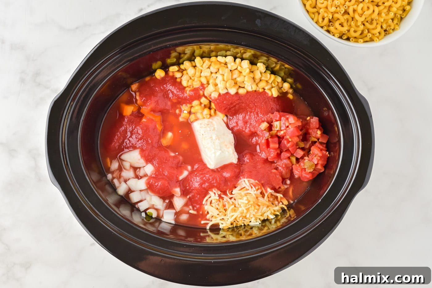 Tomato sauce, cream cheese, and various vegetables added to the crockpot with ground beef.
