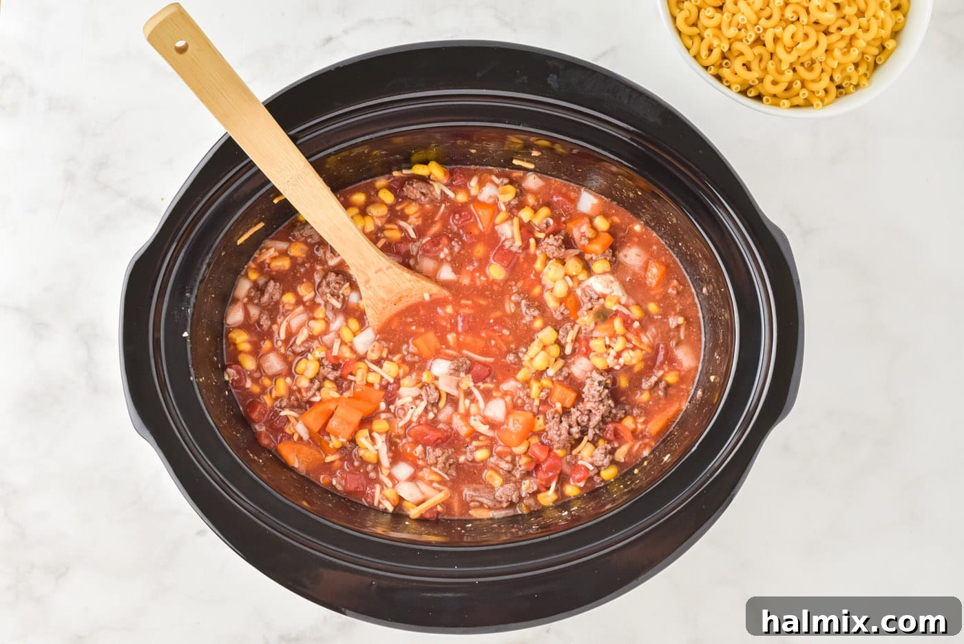 A wooden spoon stirring all the ingredients in the crockpot to combine them.