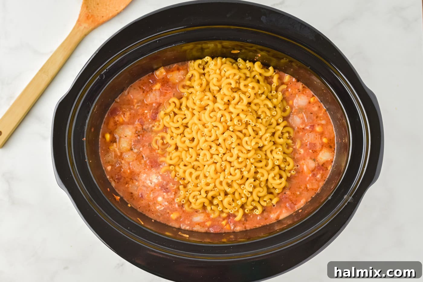 Uncooked pasta added on top of the ground beef casserole mixture in the slow cooker.