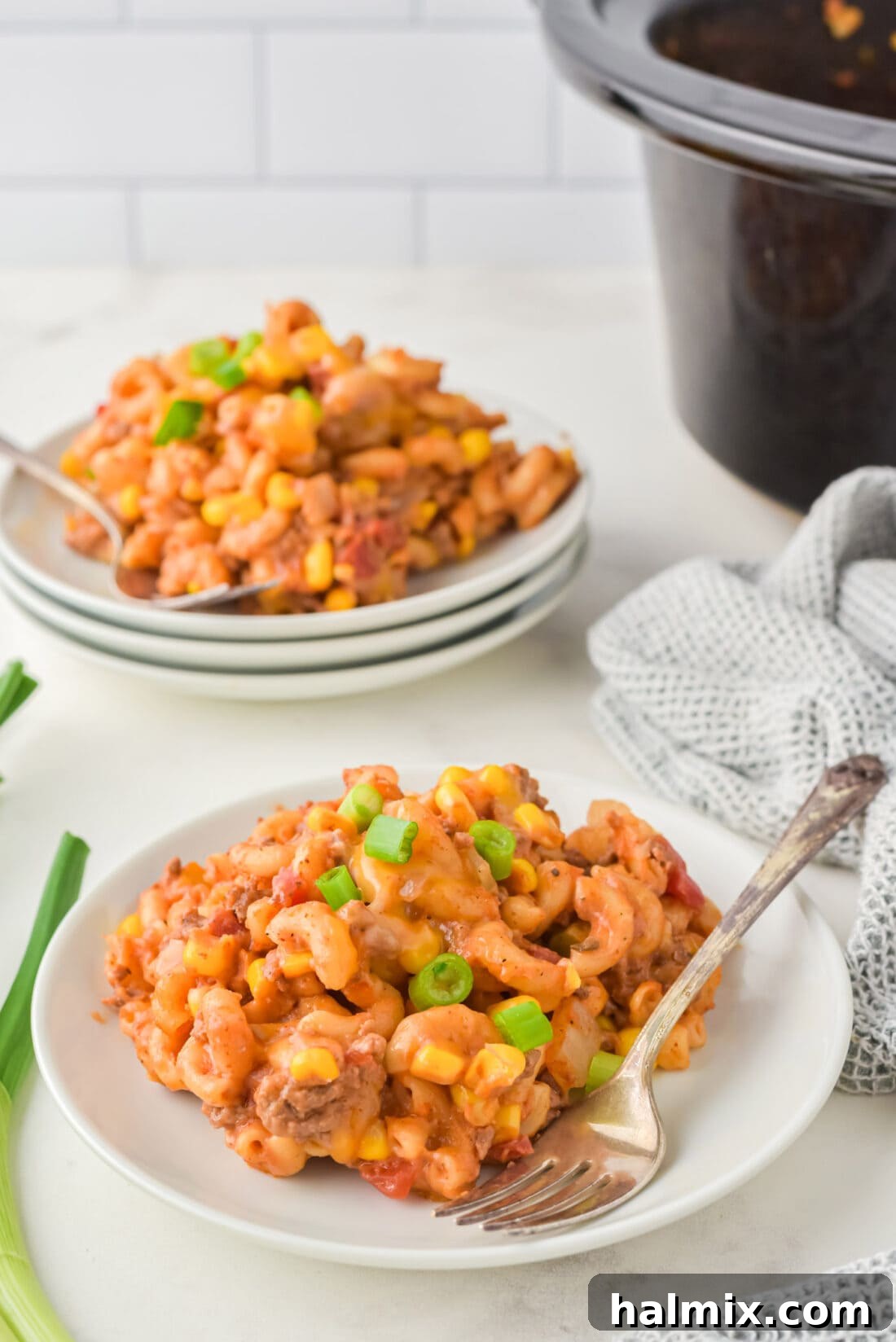 Two plates of Crockpot Ground Beef Casserole, garnished with green onions and ready to serve.