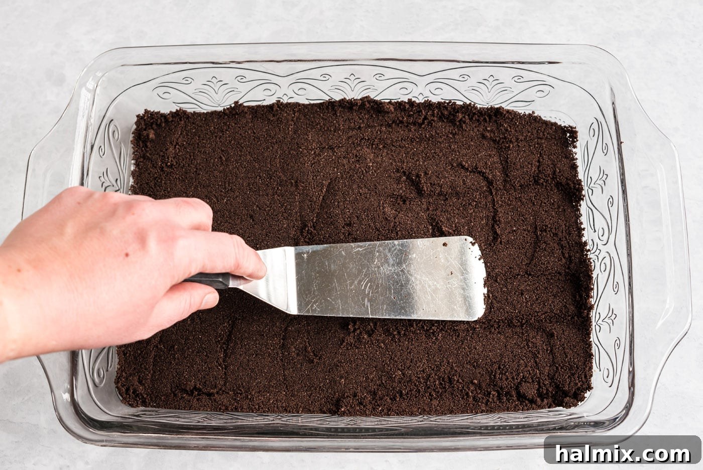 Forming the Oreo Crust in the Baking Dish Pressing Oreo crumbs into a 13x9 baking dish to form the crust
