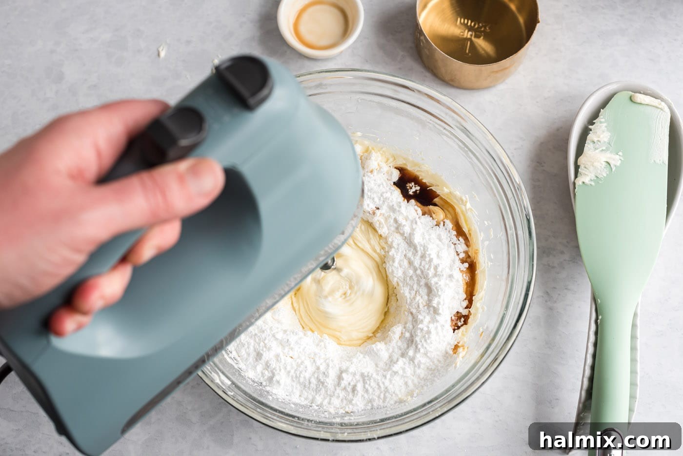 Combining Sugar and Vanilla with Cream Cheese Vanilla extract, cream cheese, and powdered sugar being mixed with a hand mixer