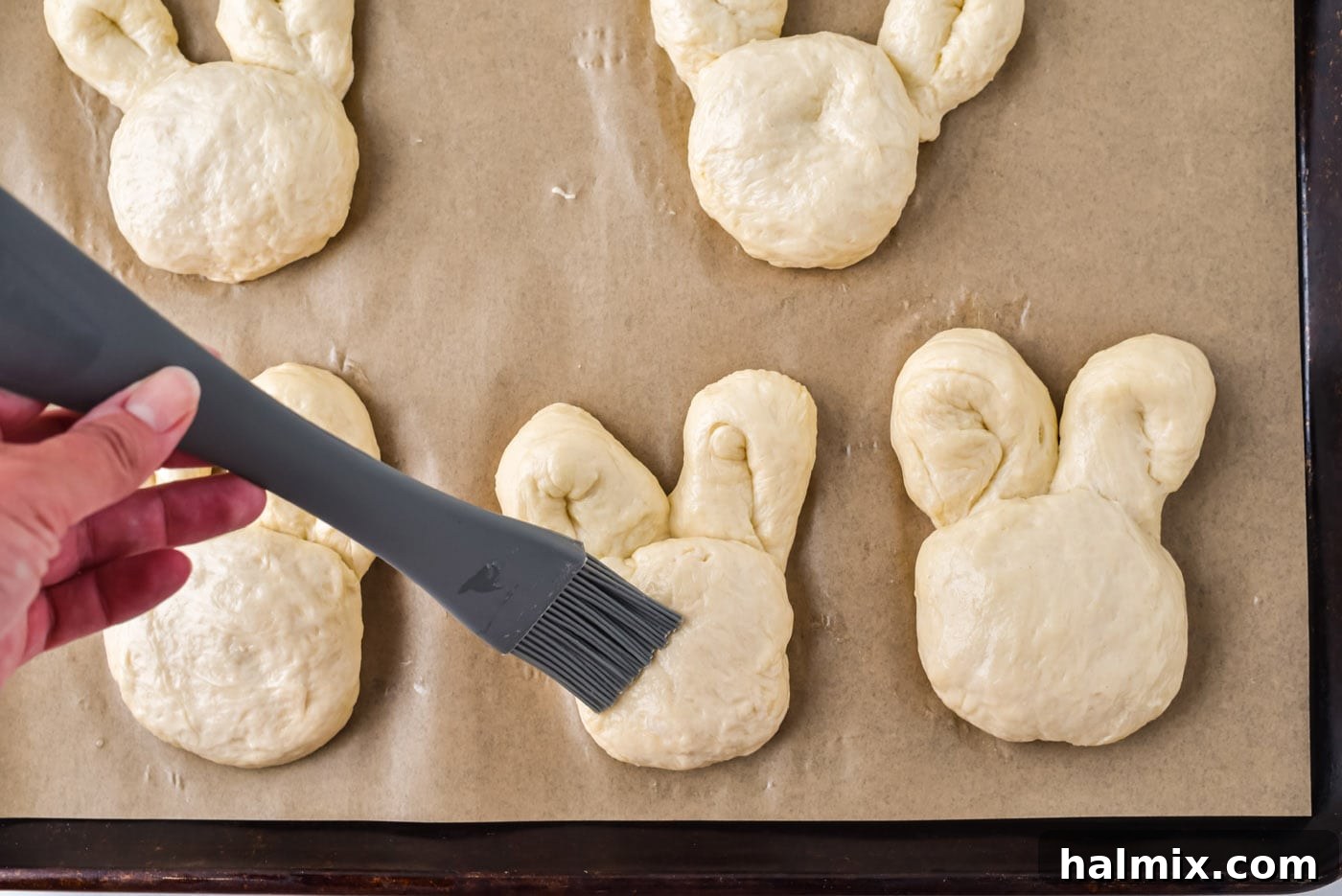 Brushing raw bunny shaped dough with an egg wash before baking.