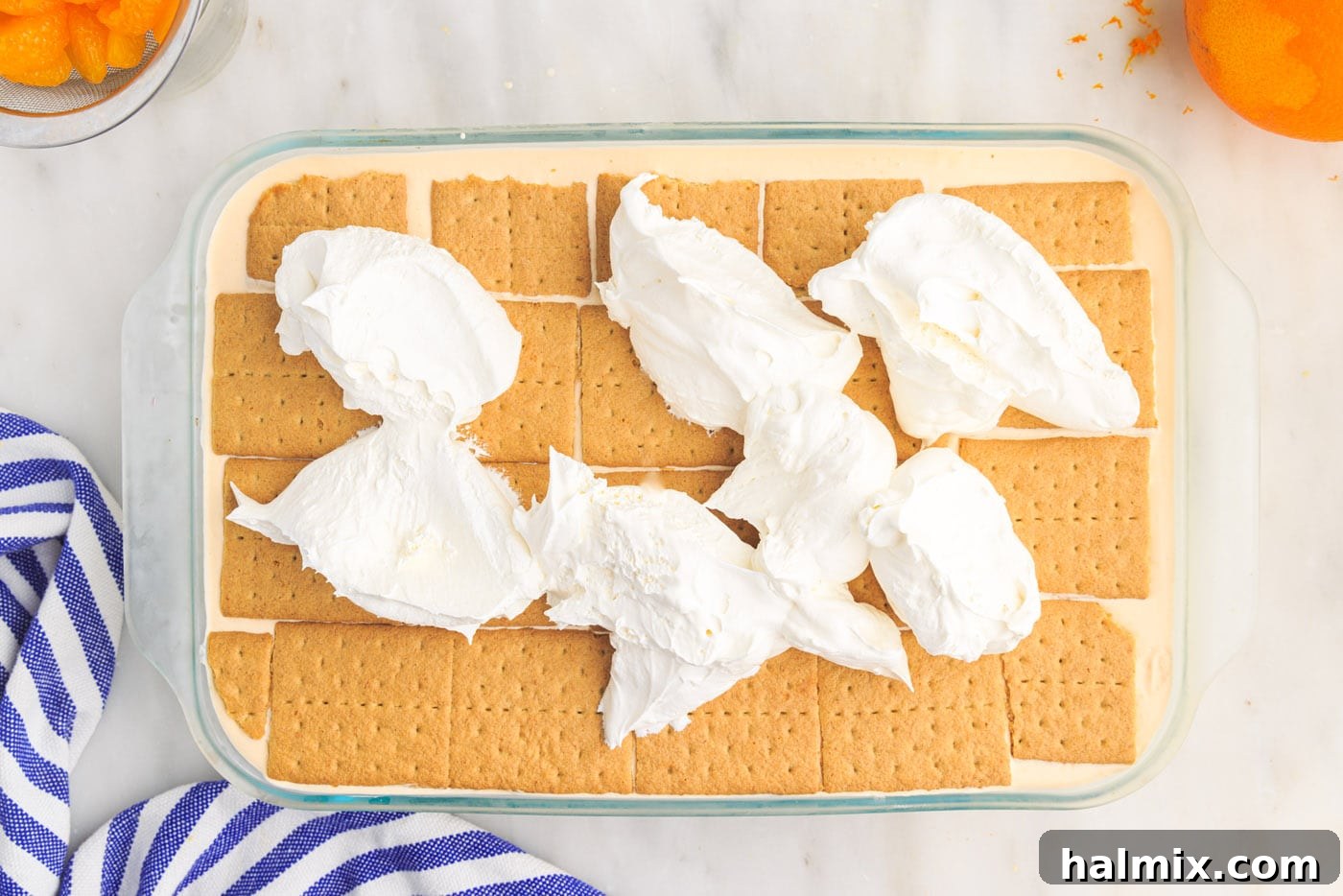 Whipped cream being spread over the top of the orange icebox cake after initial freezing