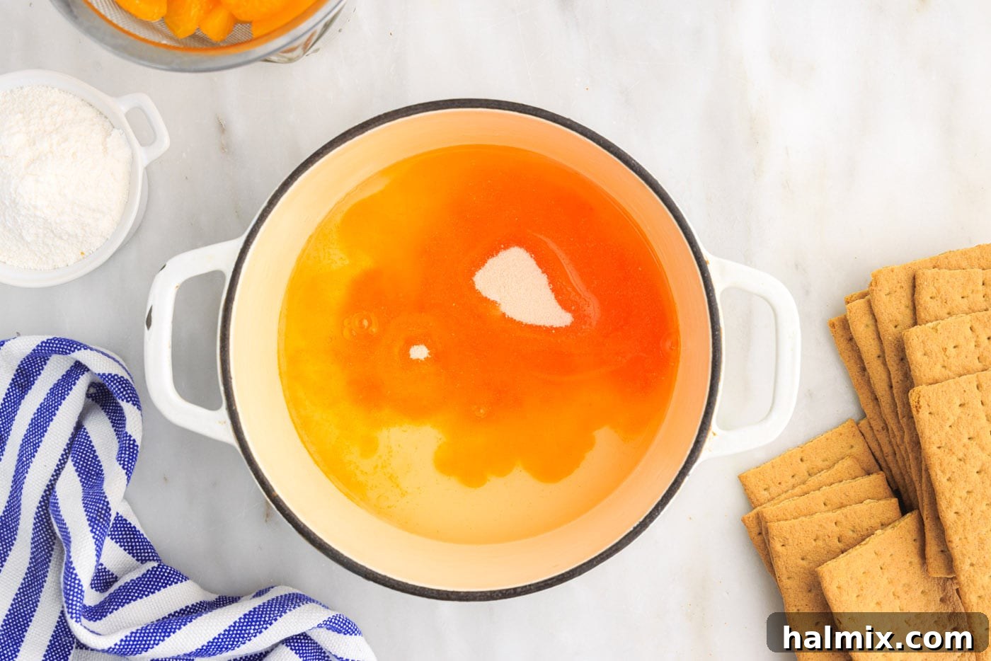 Mandarin orange juice with orange gelatin being stirred in a saucepan