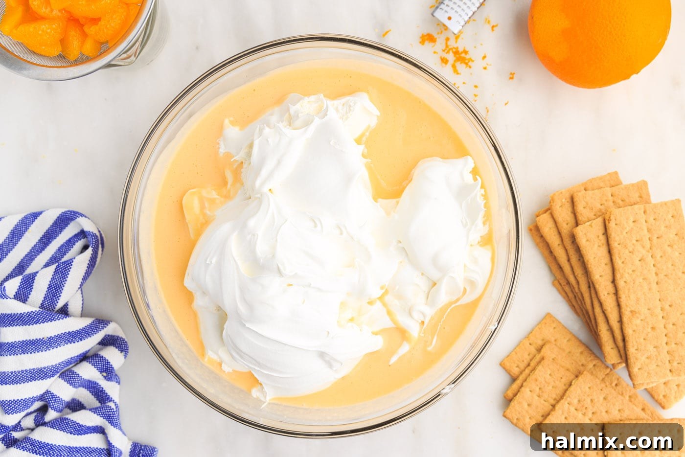 Cool Whip added on top of the orange pudding mixture in a mixing bowl