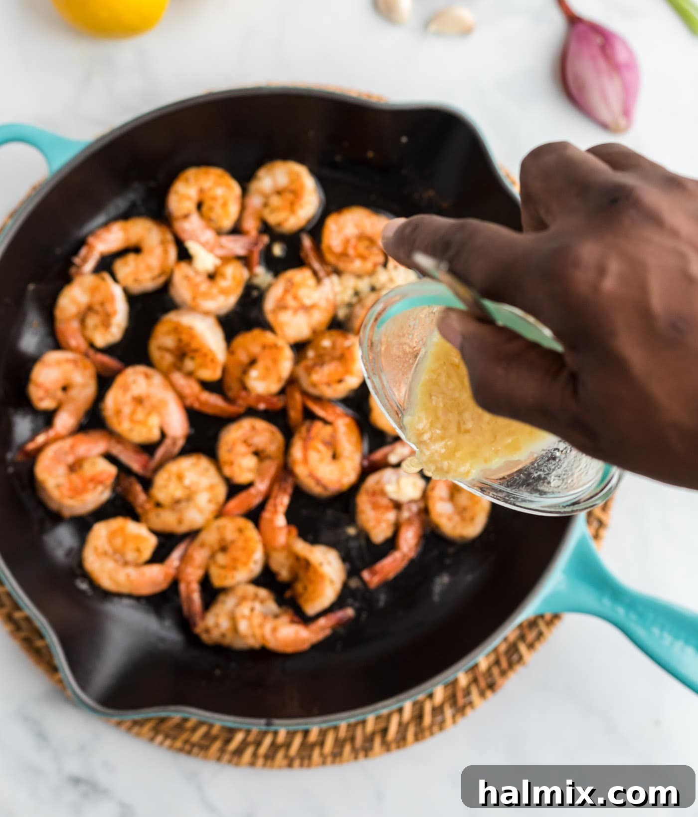 Pouring the garlic butter sauce over sautéed shrimp in a skillet.
