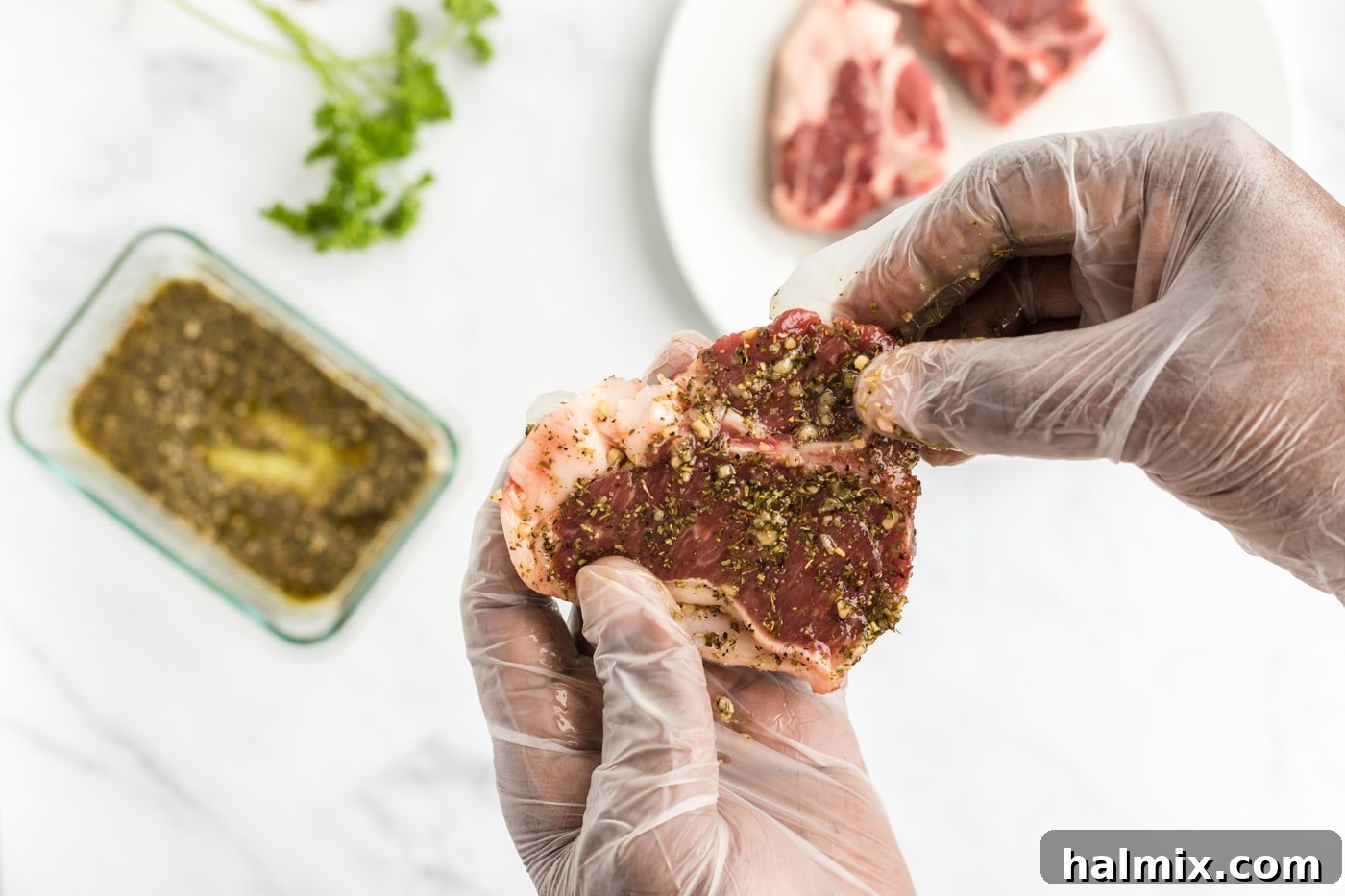 Hands gently massaging the wet rub onto a lamb chop, ensuring full coverage.