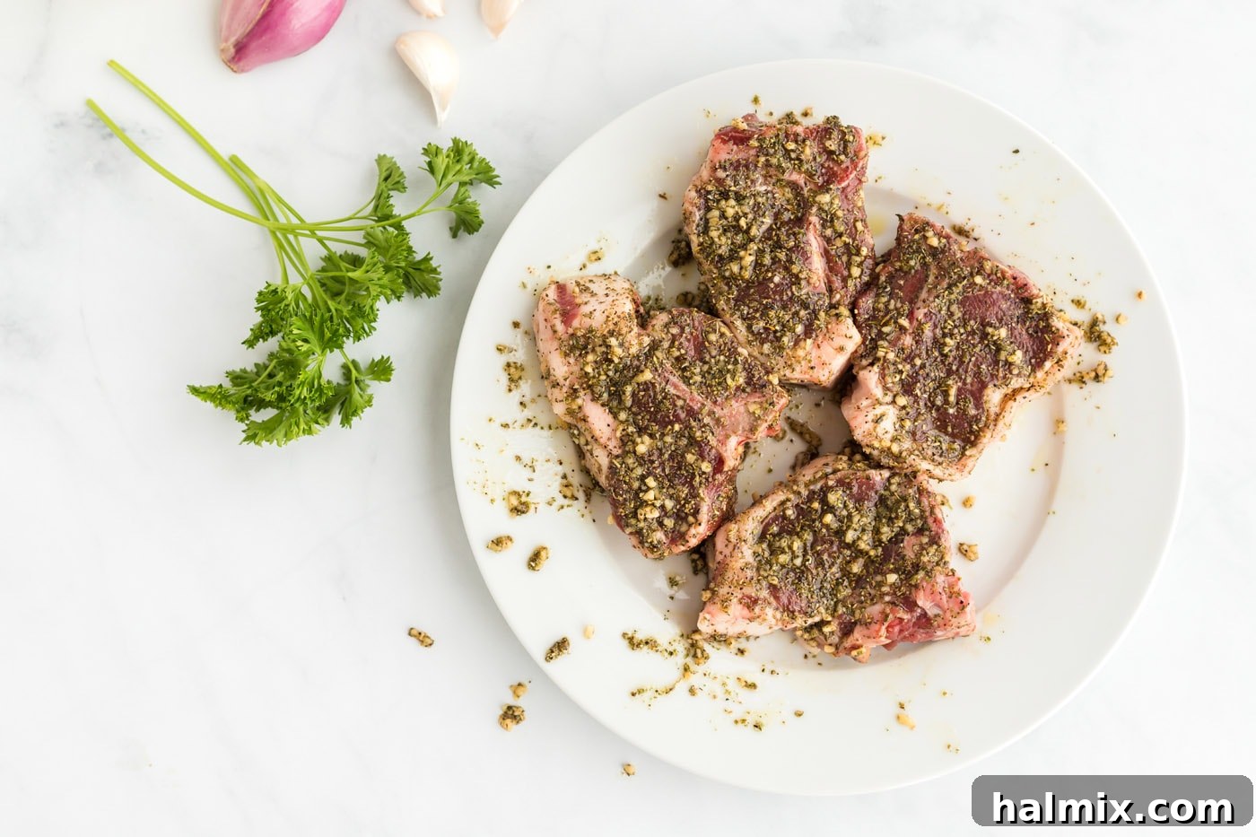 Marinated lamb chops arranged on a plate, fully coated in the herb and garlic rub, ready for searing.