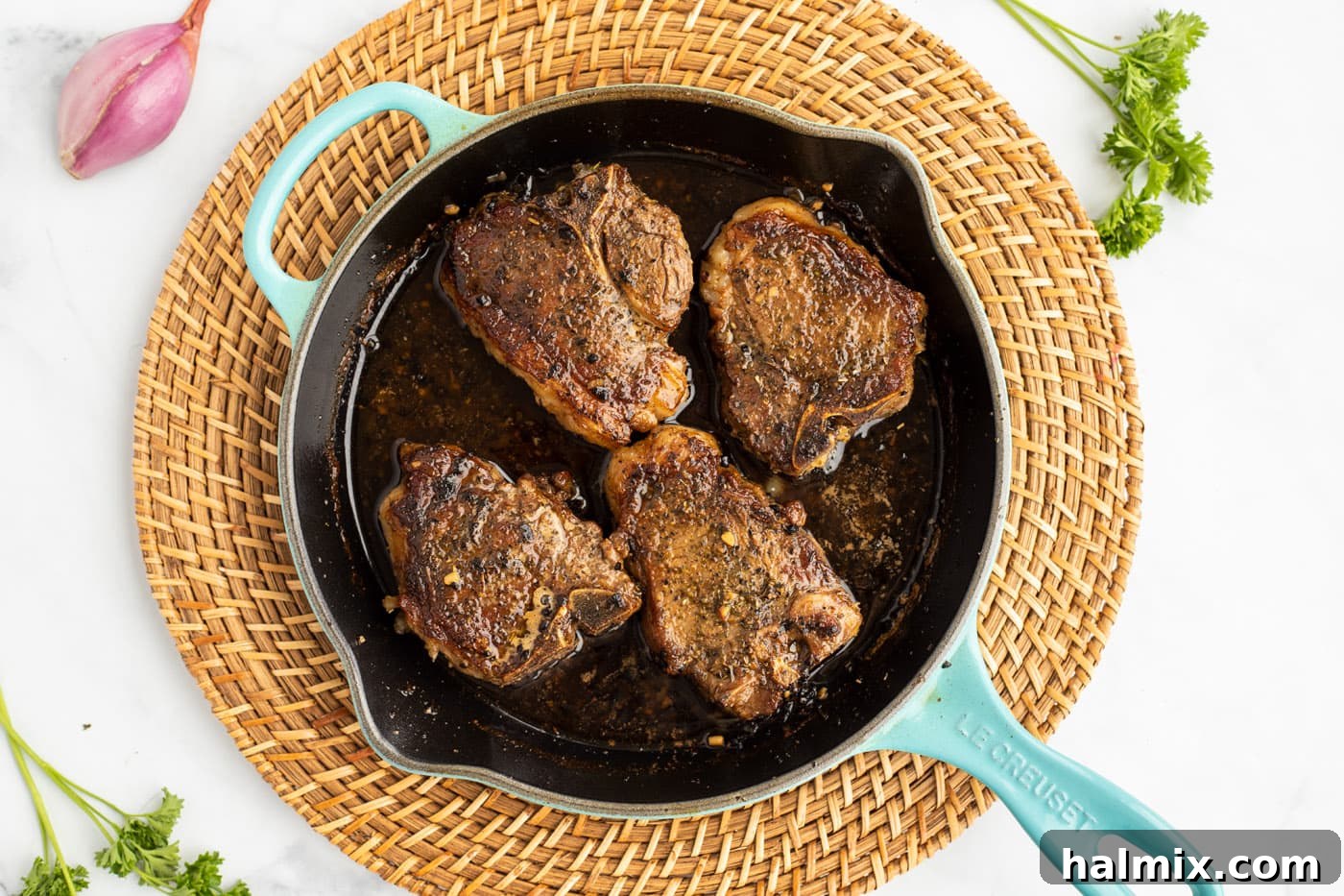 Lamb chops simmering in the white wine reduction inside an oven-safe skillet, ready for the oven.