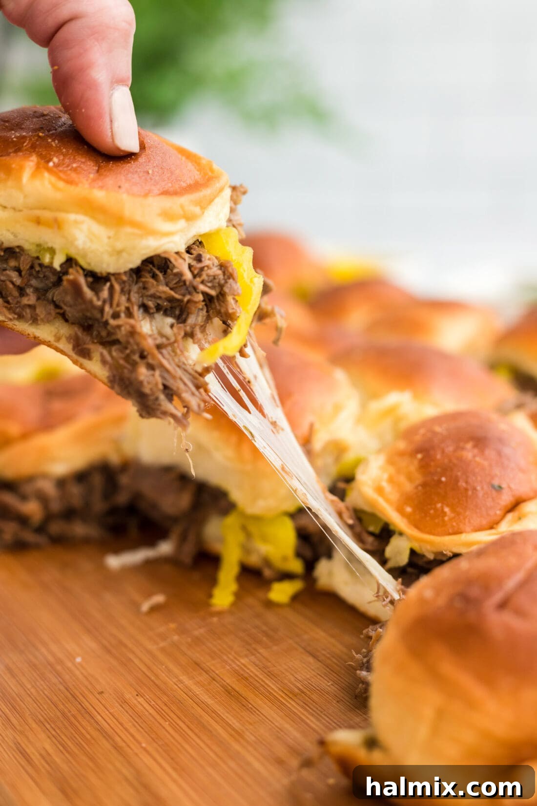 A hand lifting a Mississippi Pot Roast Slider from a baking pan, showcasing the melted cheese and tender meat.