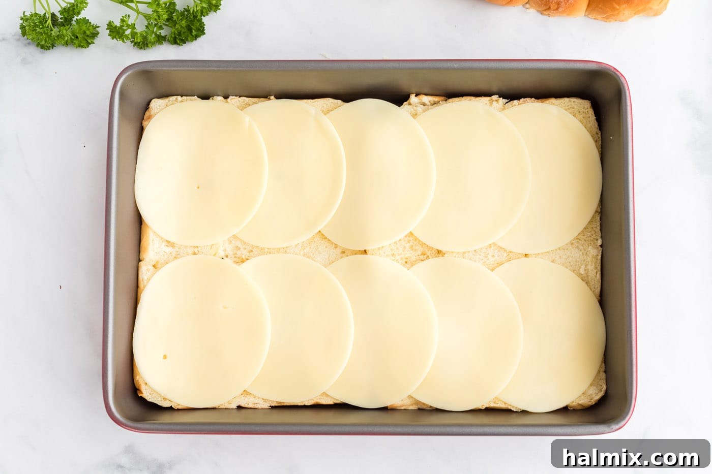 Slices of provolone cheese layered over the bottom halves of Hawaiian rolls in the baking pan.