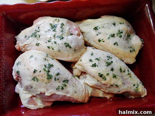 An overhead view of unroasted chicken breasts, seasoned with fresh lemon thyme leaves, placed in a red roasting pan, ready for the oven.