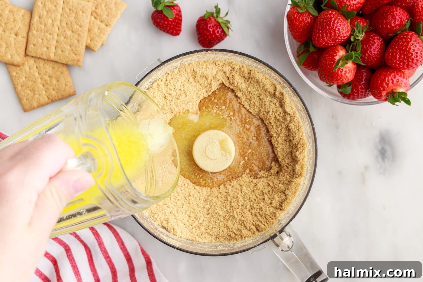 Strawberry Lasagna Delight 7 Melted butter being poured over graham cracker crumbs in a food processor, ready to be combined.