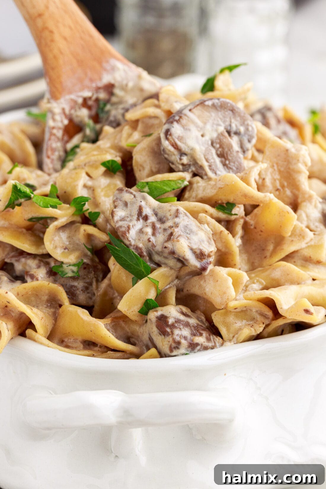 Wooden spoon lifting out a generous portion of Instant Pot Beef Stroganoff, showcasing the tender beef and creamy noodles.