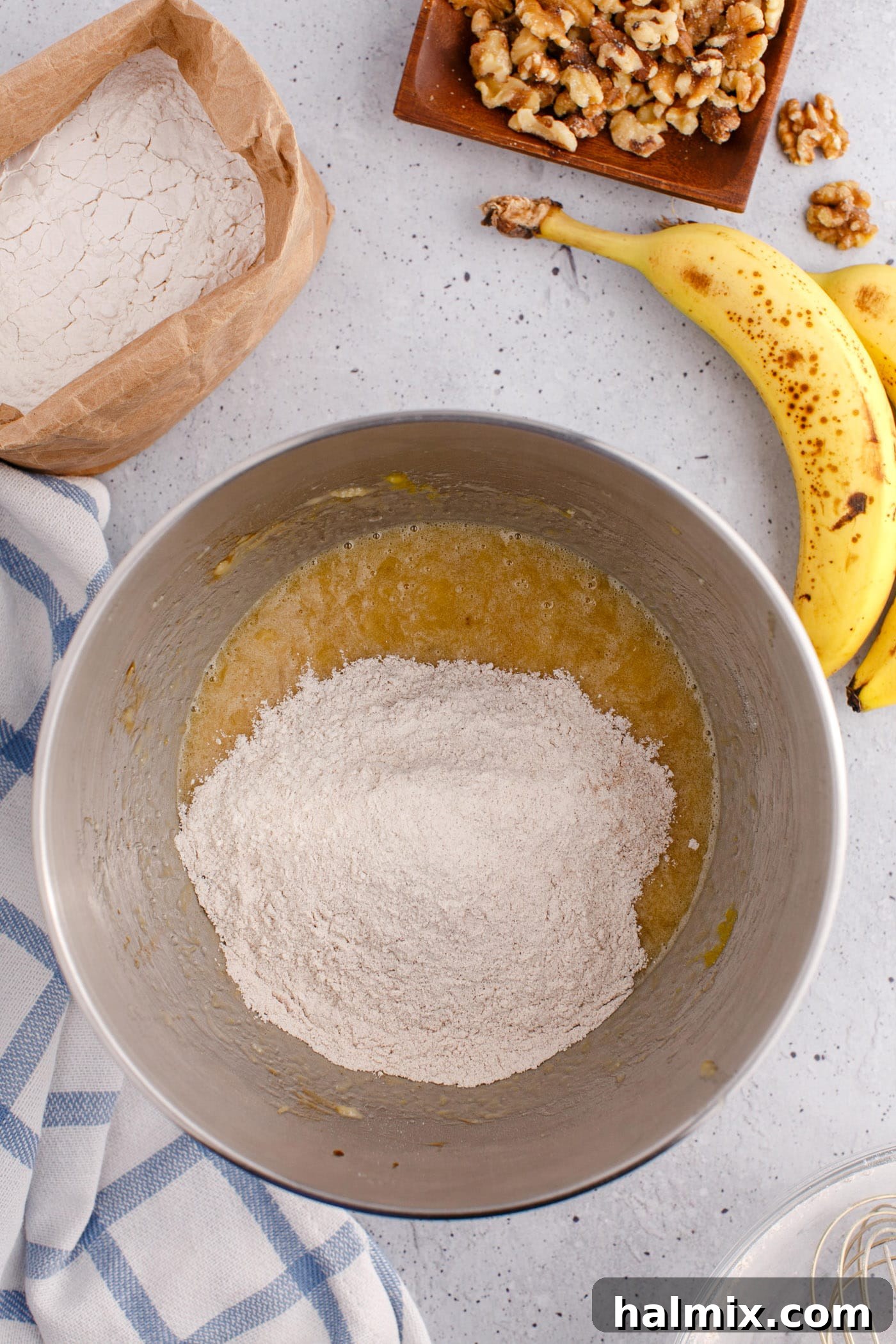 flour mixture being added to the wet banana bread ingredients in a mixing bowl