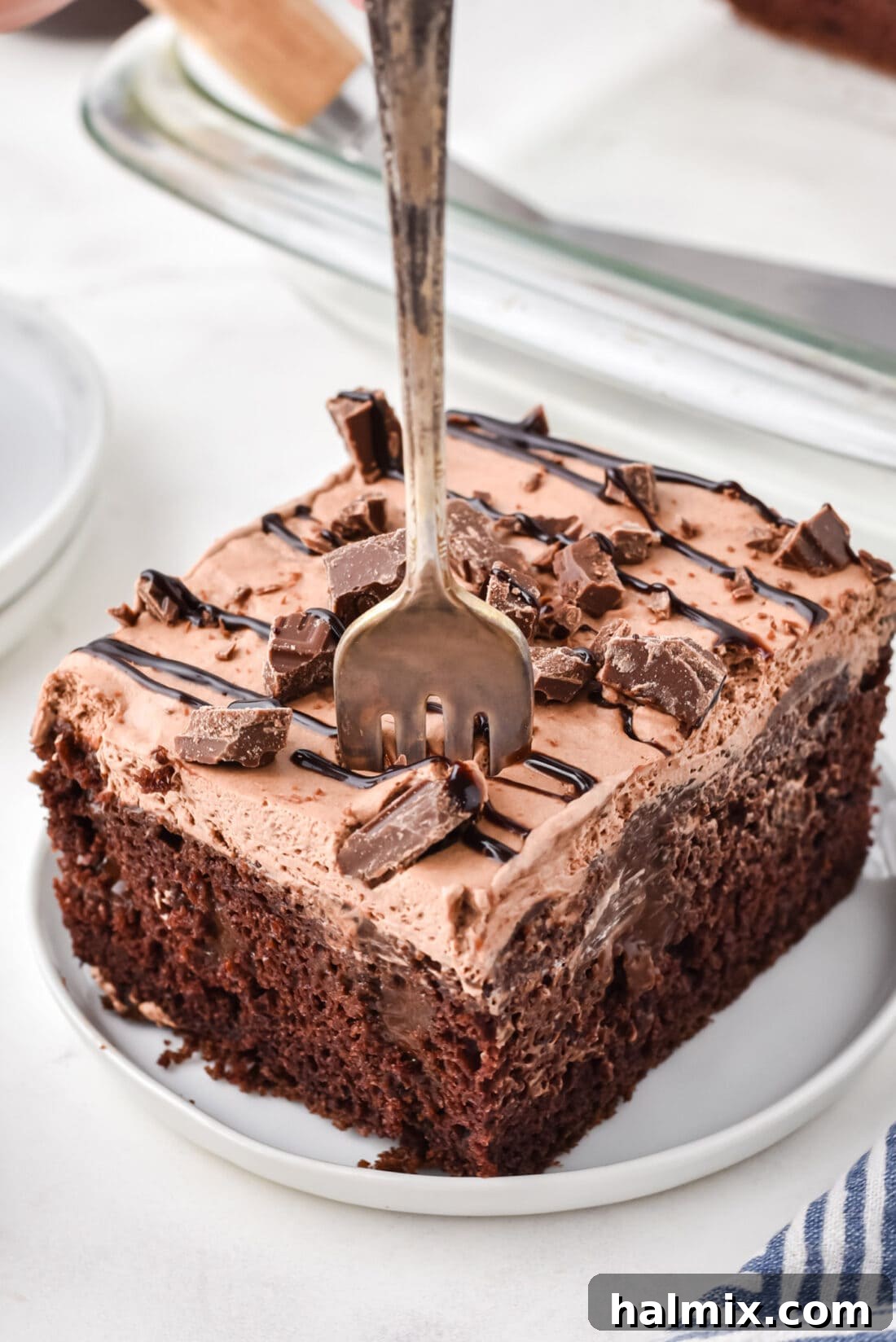 A close-up shot of a fork digging into a slice of Chocolate Poke Cake, showing its moist, layered texture and inviting richness.