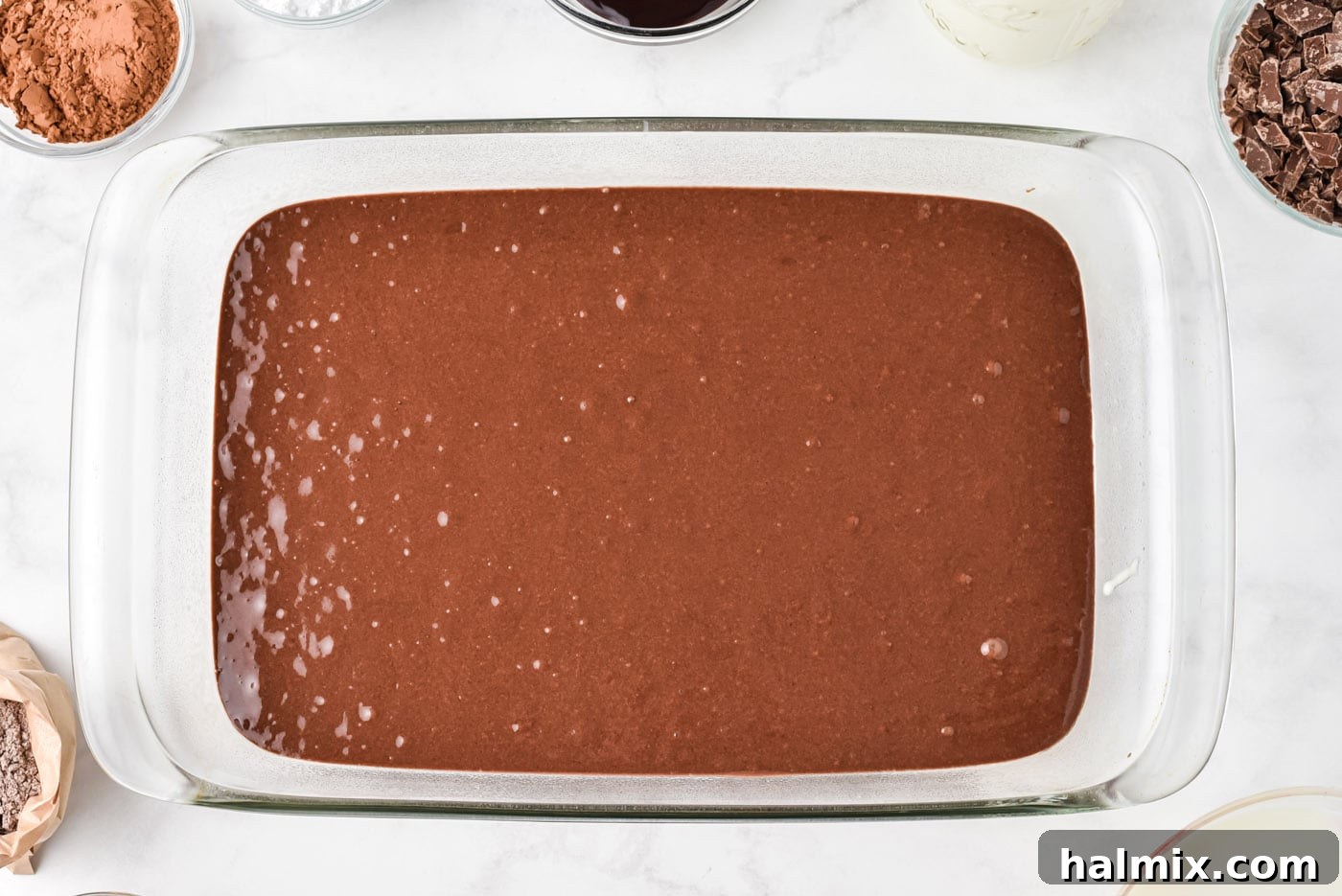 Smooth devil's food cake batter poured into a clear 13x9 inch baking dish, ready for baking.