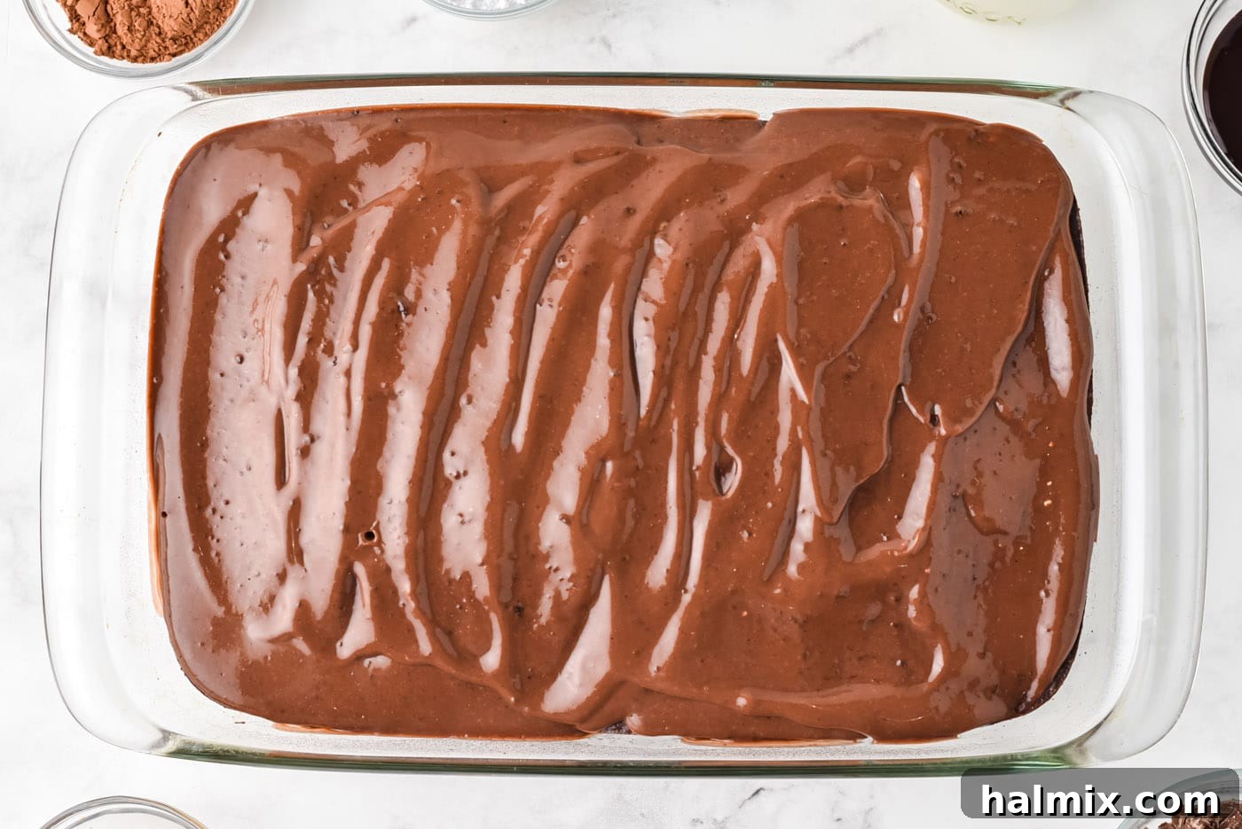 Chocolate pudding fully covering the surface of the poke cake, visibly filling the holes and creating a smooth, rich top layer.