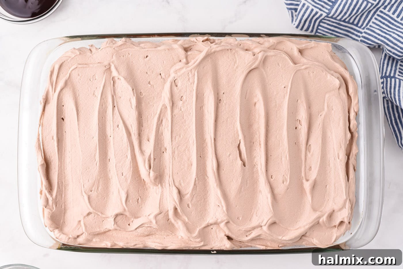 Chocolate poke cake fully covered with a smooth, even layer of chocolate whipped cream, looking rich and ready for final garnishes.