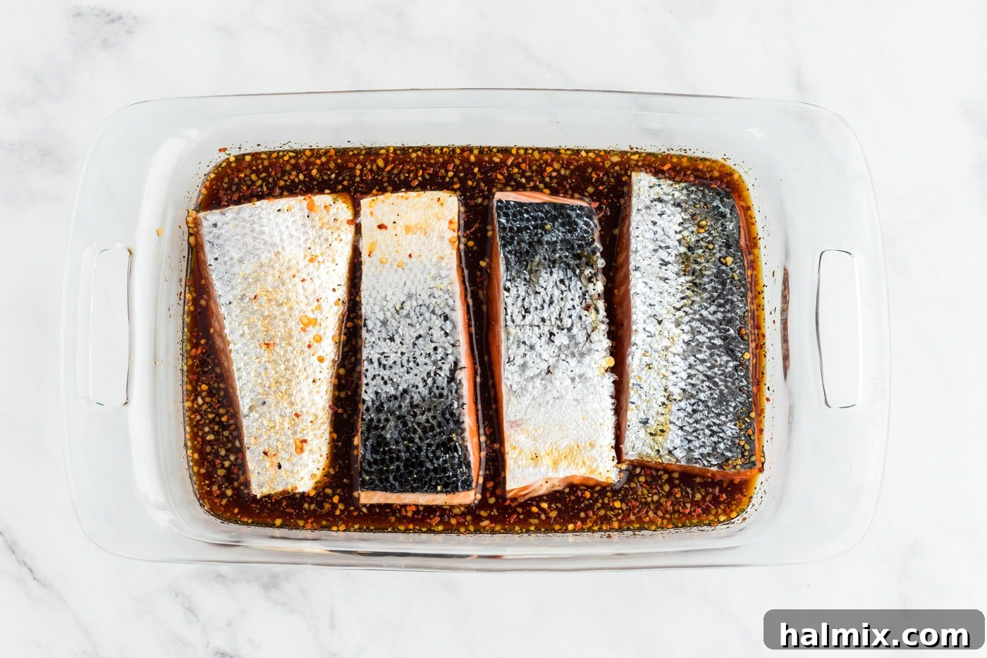 Salmon fillets marinating in maple syrup and soy sauce mixture in a baking dish.