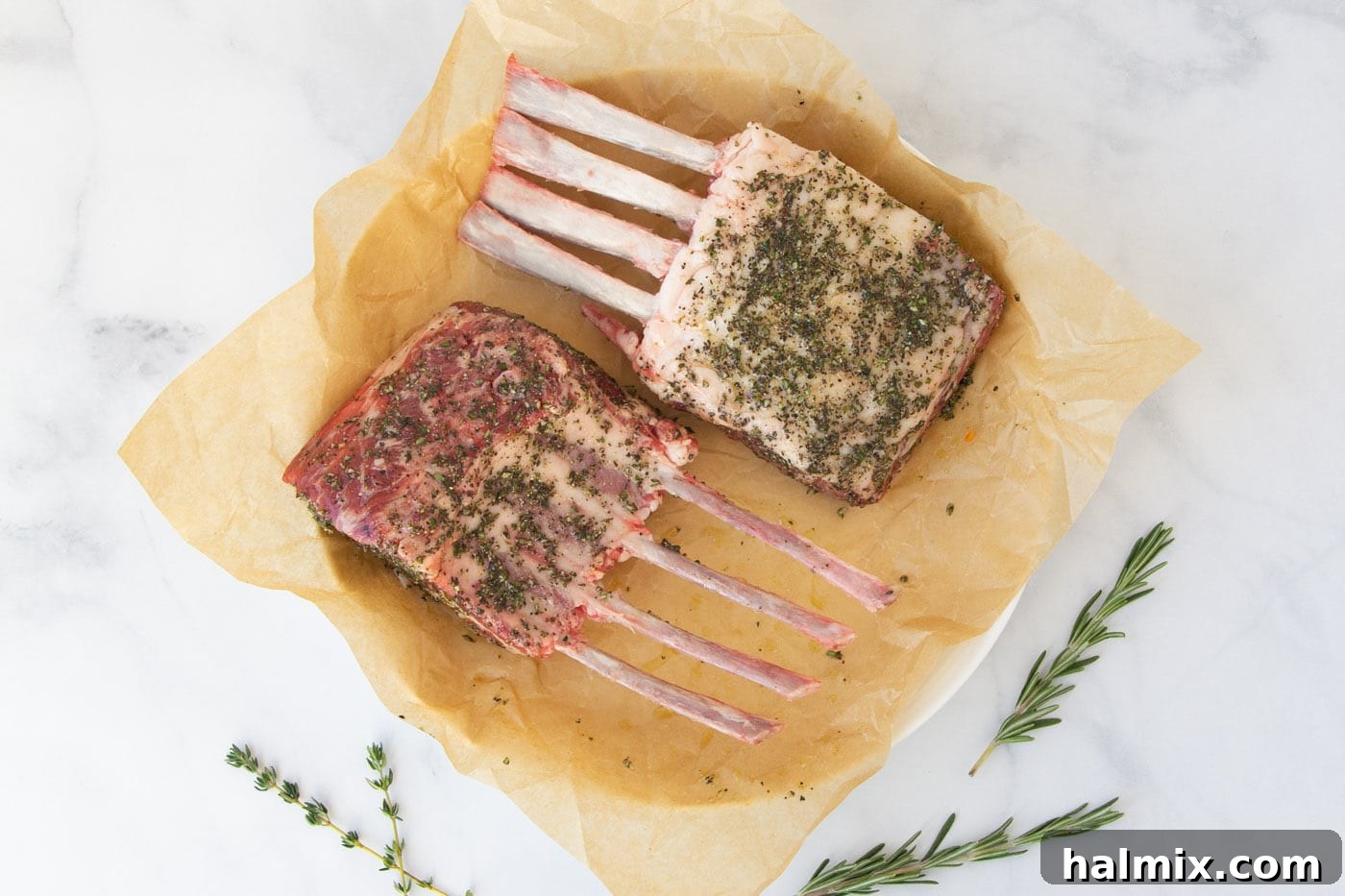Rack of lamb marinating in a glass pan, covered with a plastic wrap, soaking in the herb and spice rub.