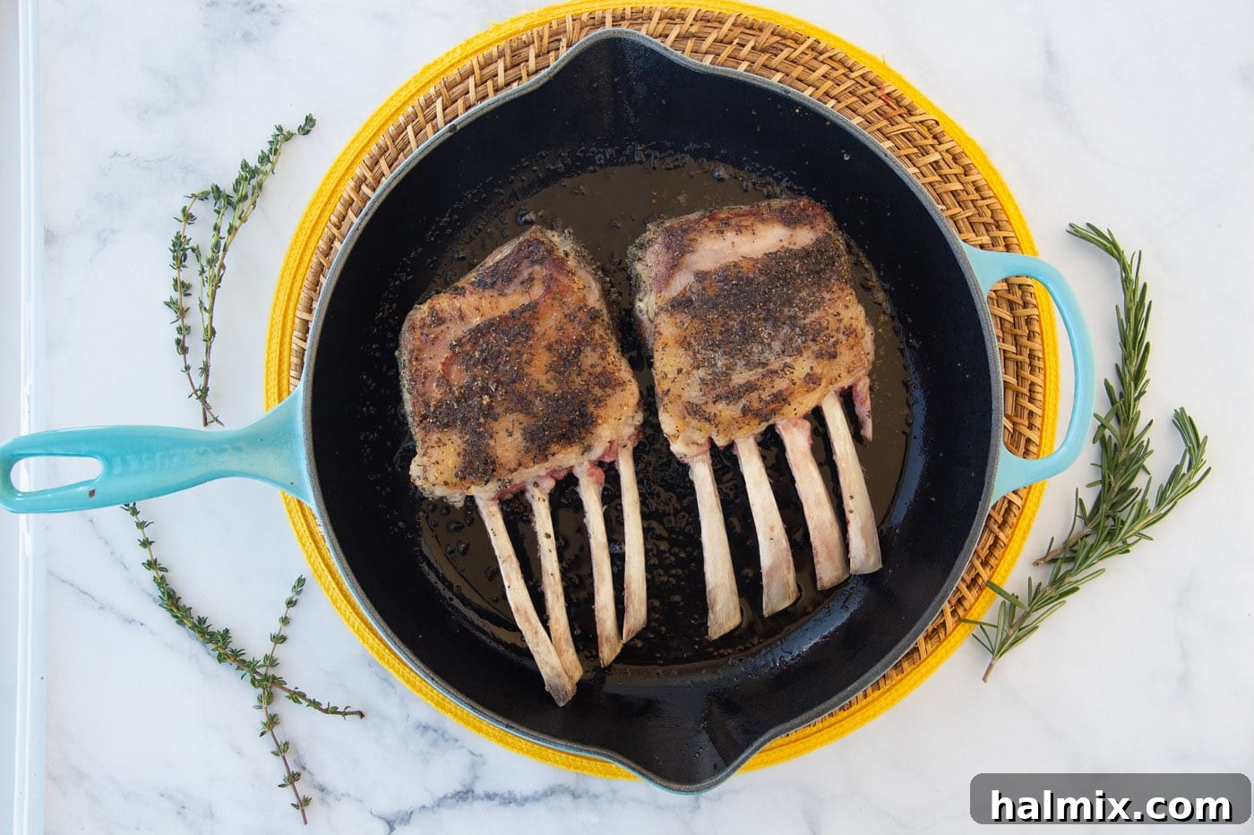 Rack of lamb searing in a hot skillet, developing a golden-brown crust on the fat side.