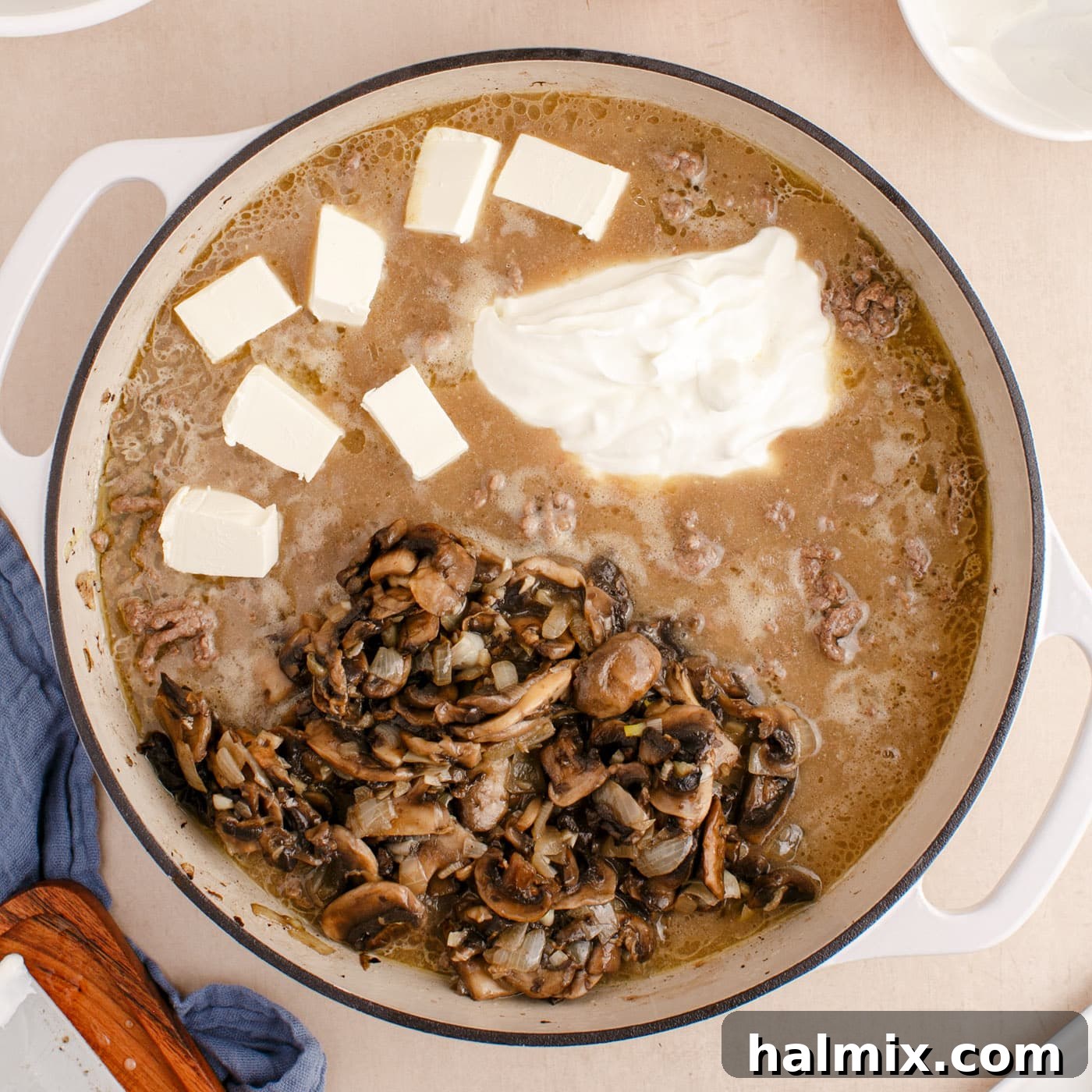 Creamy Ground Beef Stroganoff 9 Mushrooms, cream cheese, and sour cream being stirred into the creamy ground beef stroganoff sauce in the skillet.