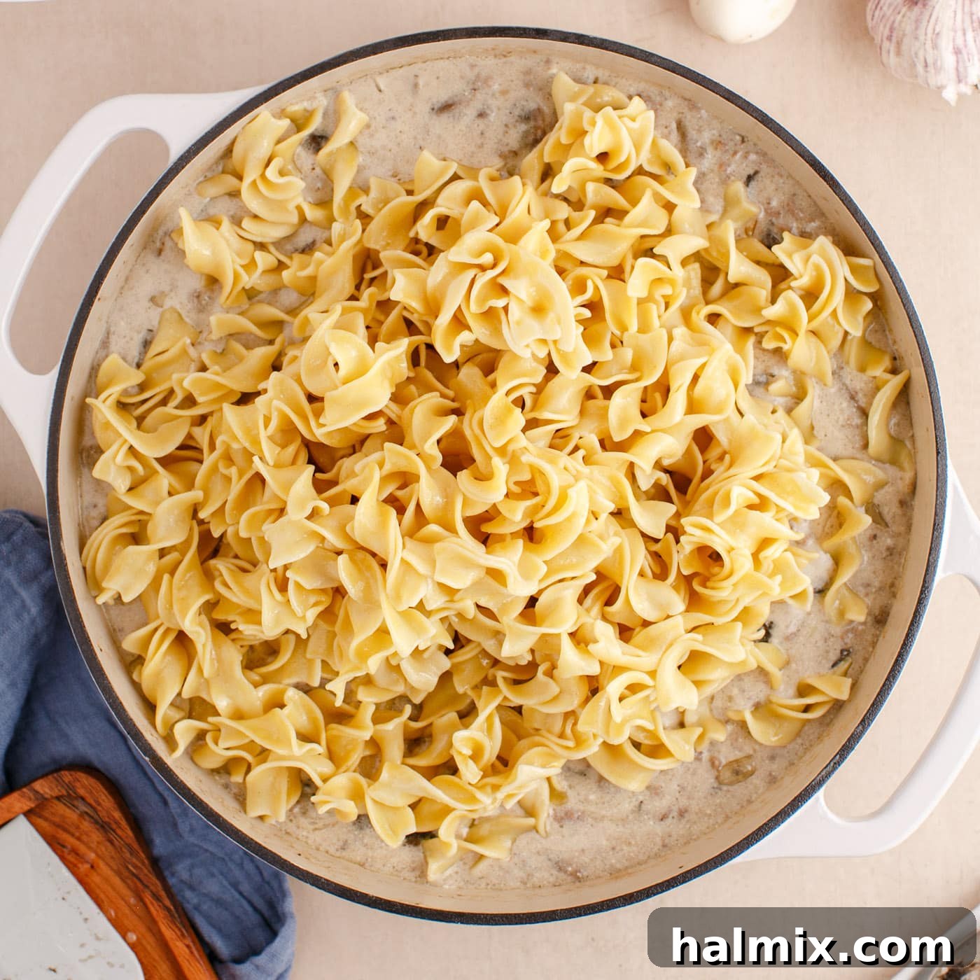 Creamy Ground Beef Stroganoff 10 Cooked wide egg noodles being added on top of the ground beef stroganoff in the skillet, ready to be mixed.