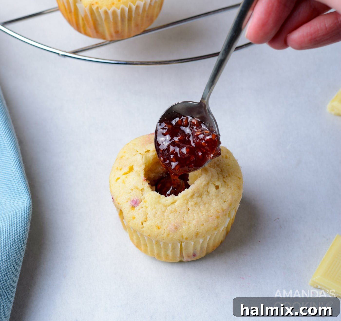Raspberry jam being spooned into the hollowed center of a cupcake
