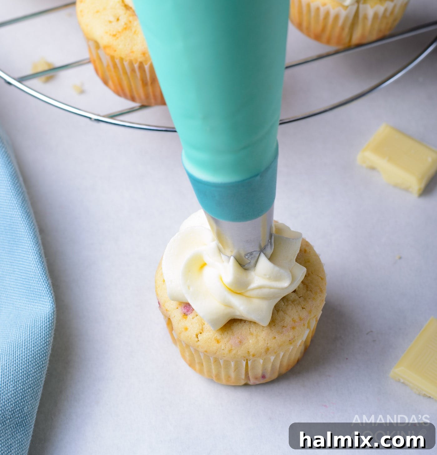 White chocolate buttercream being piped onto a raspberry-filled cupcake