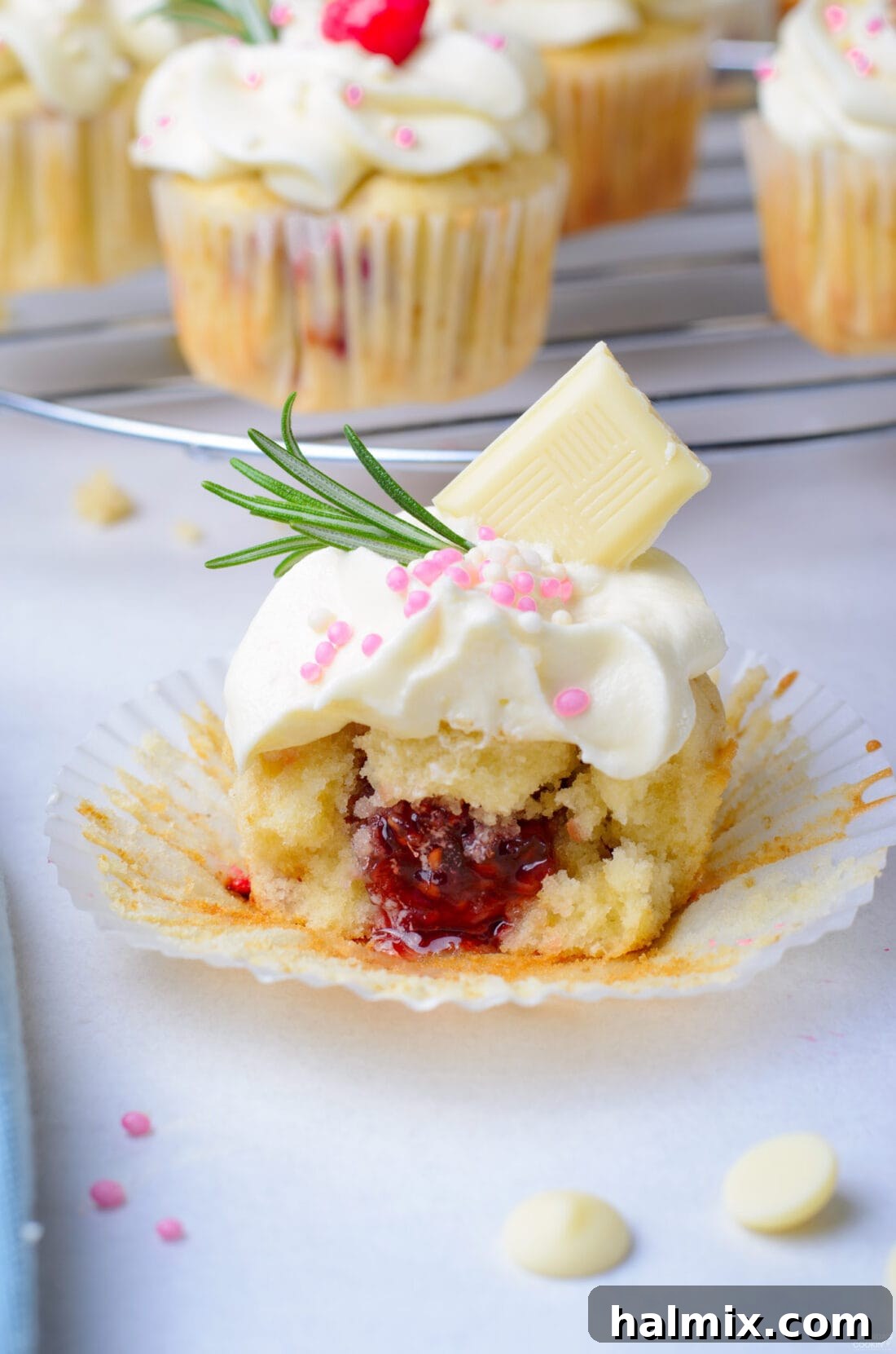 A Raspberry White Chocolate Cupcake cut in half, showcasing its fluffy interior and vibrant raspberry jam filling