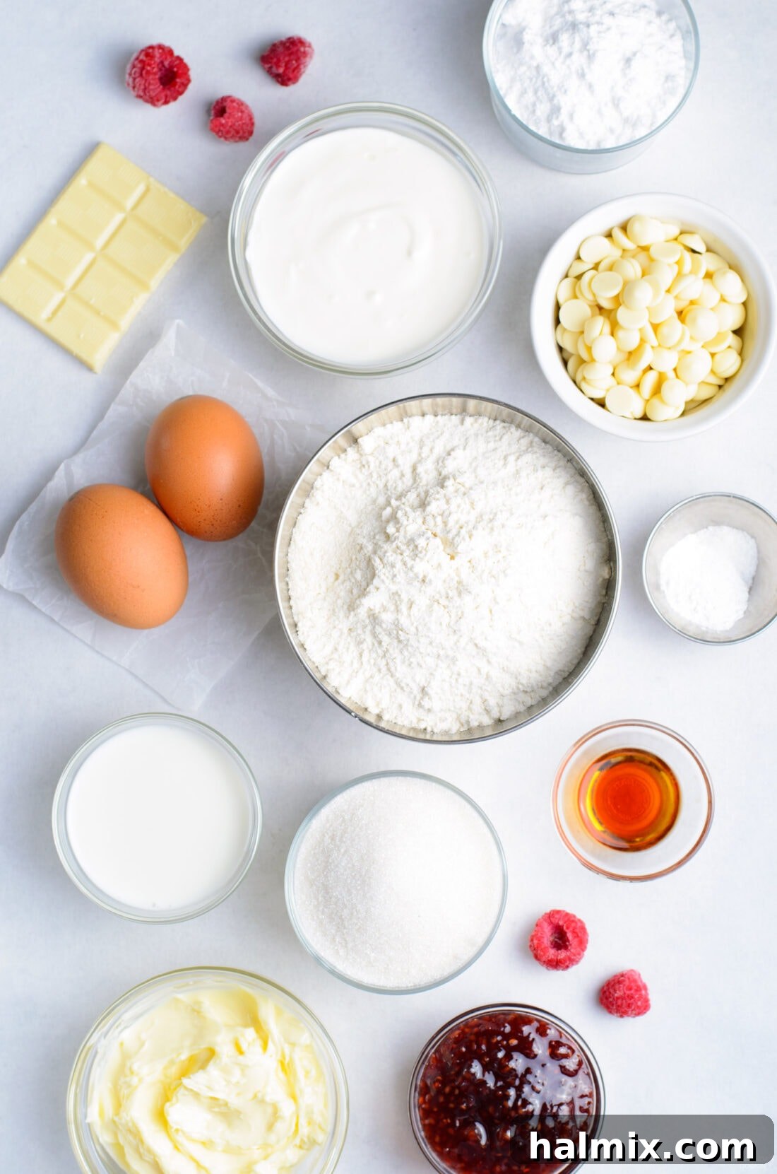 Various ingredients laid out for making Raspberry White Chocolate Cupcakes, including flour, butter, eggs, raspberries, and white chocolate chips