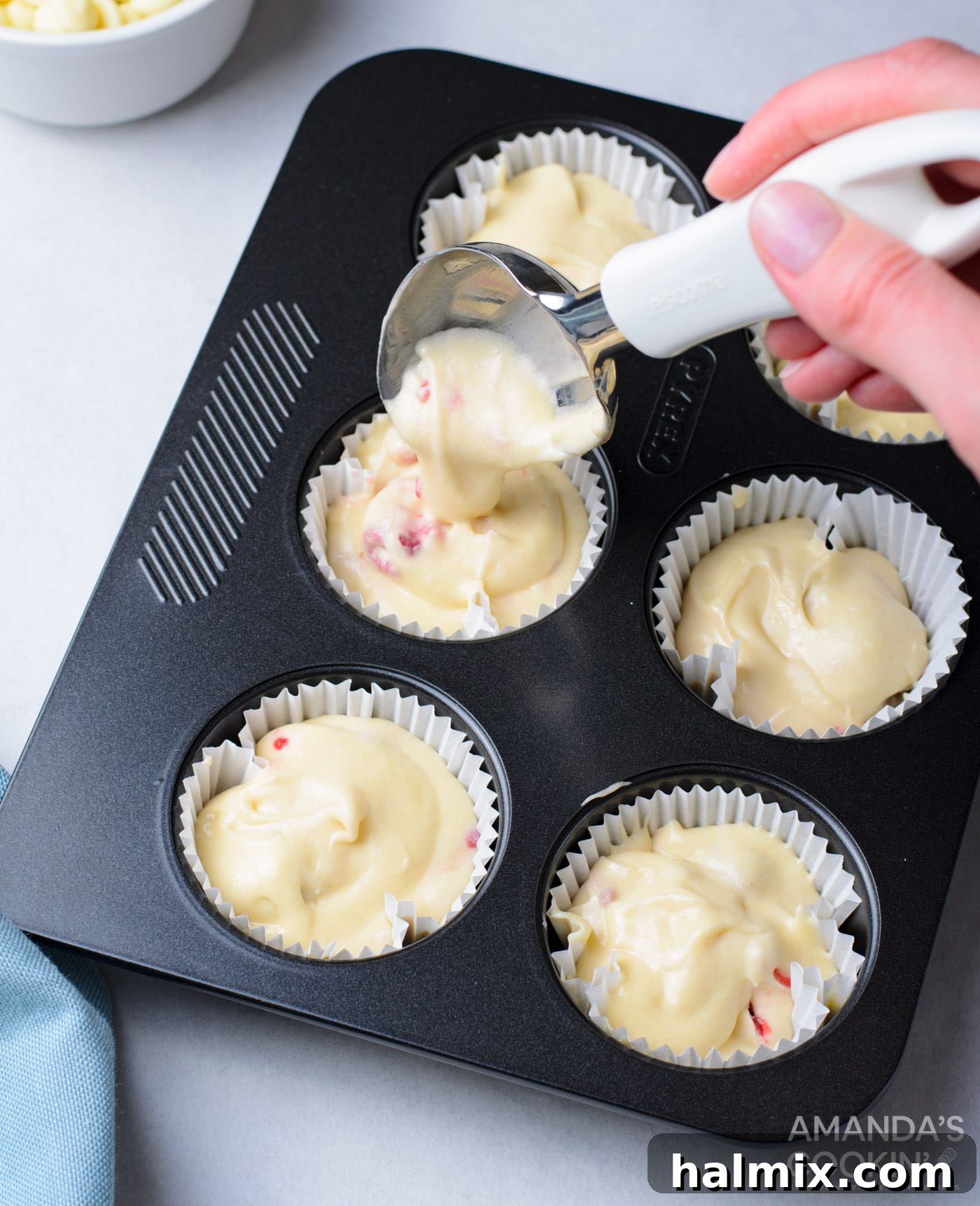 Cupcake liners being filled with raspberry cupcake batter using a spoon