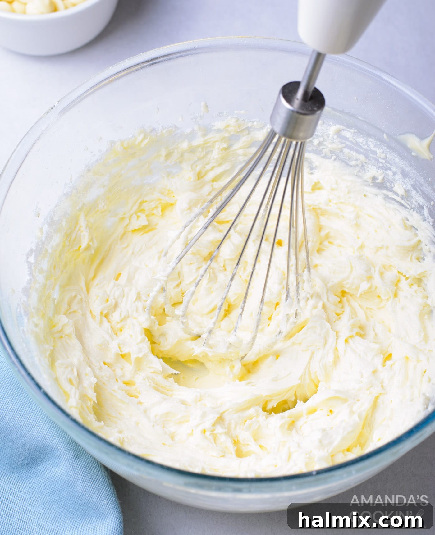 Butter and powdered sugar being mixed in a bowl with an electric mixer to create fluffy buttercream frosting