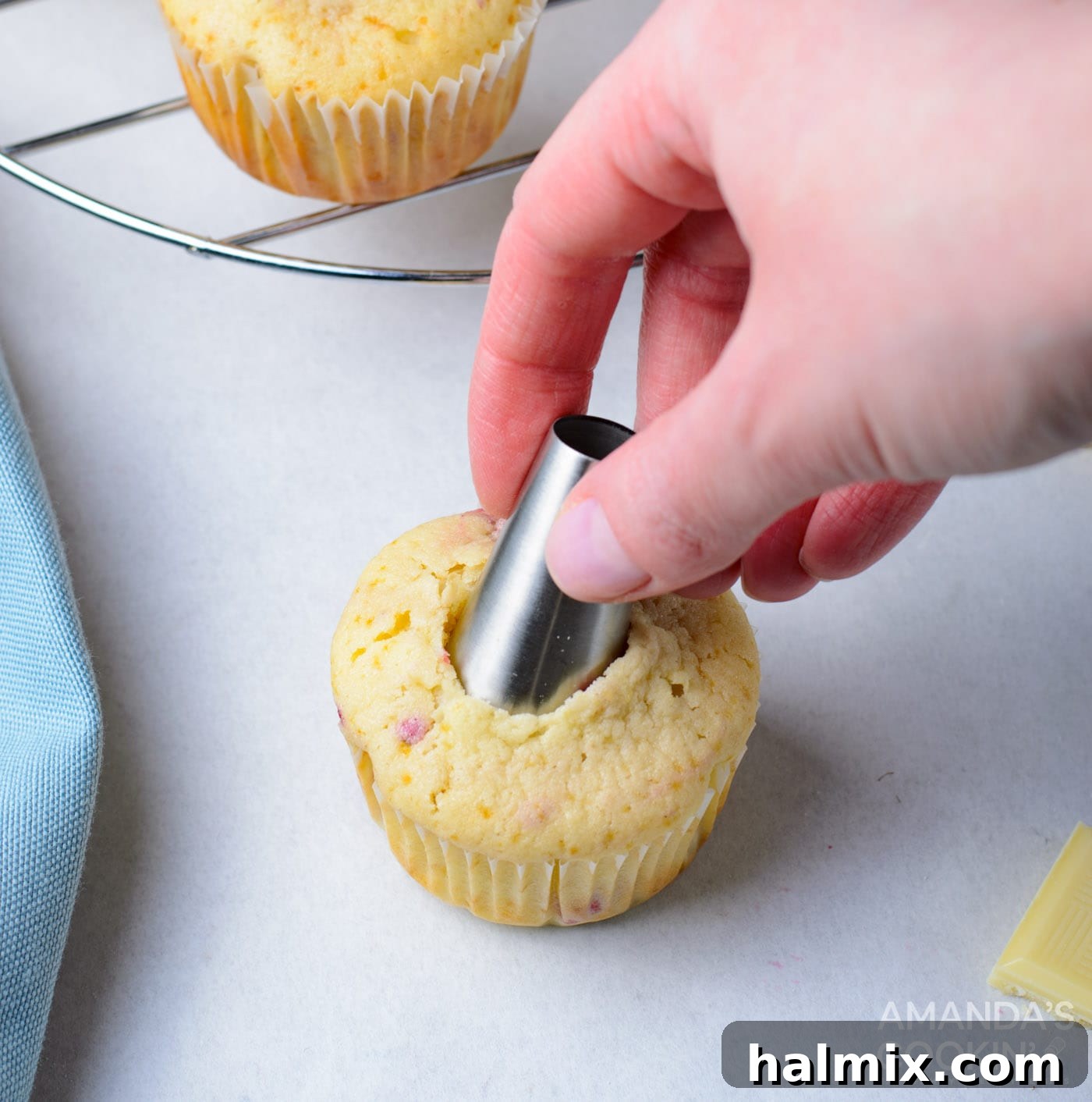 A piping tip being used to create a small hole in the center of a cooled cupcake for filling