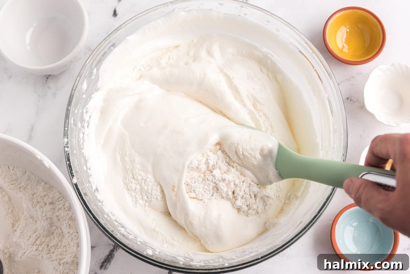 Feather-Light Angel Food Cake 9 Folding flour mixture into egg white mixture in a bowl with a rubber spatula, demonstrating a light touch