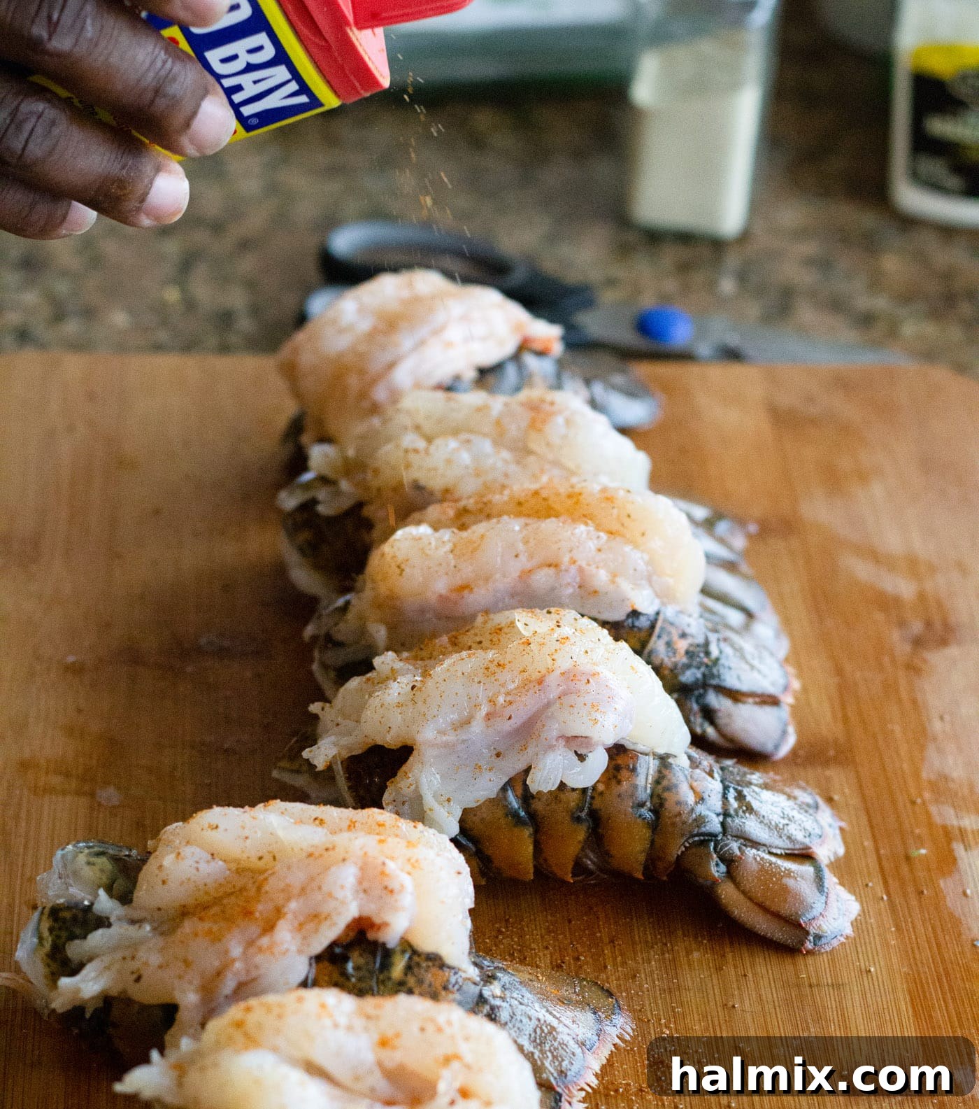 Seasoning raw lobster tails with Old Bay before cooking to enhance flavor
