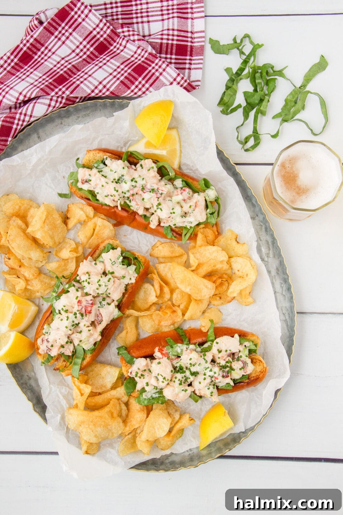 Three perfectly presented lobster rolls arranged on a large platter with a generous side of potato chips