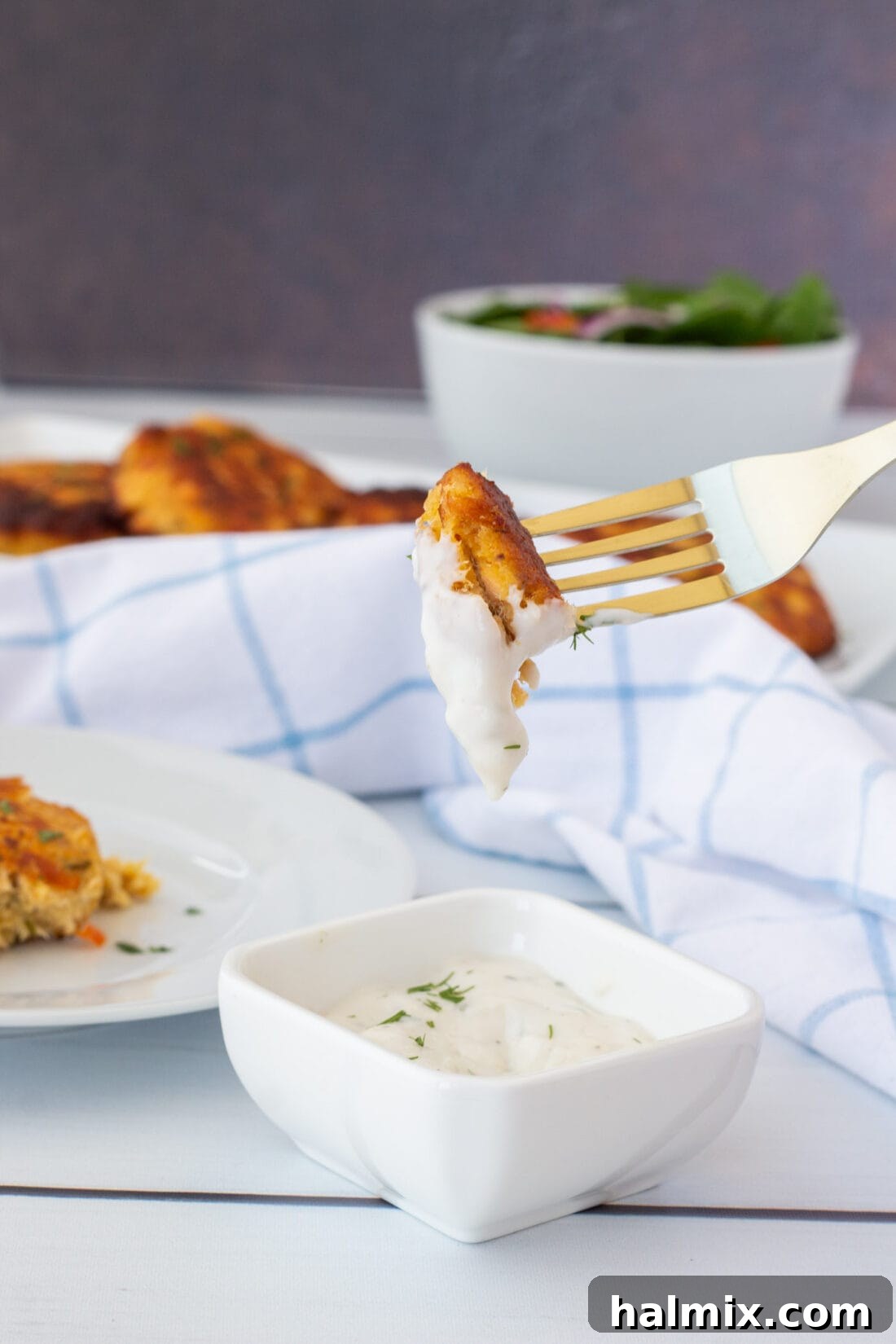 A fork holding a piece of smoked salmon fish cake, dipped in a creamy white sauce.