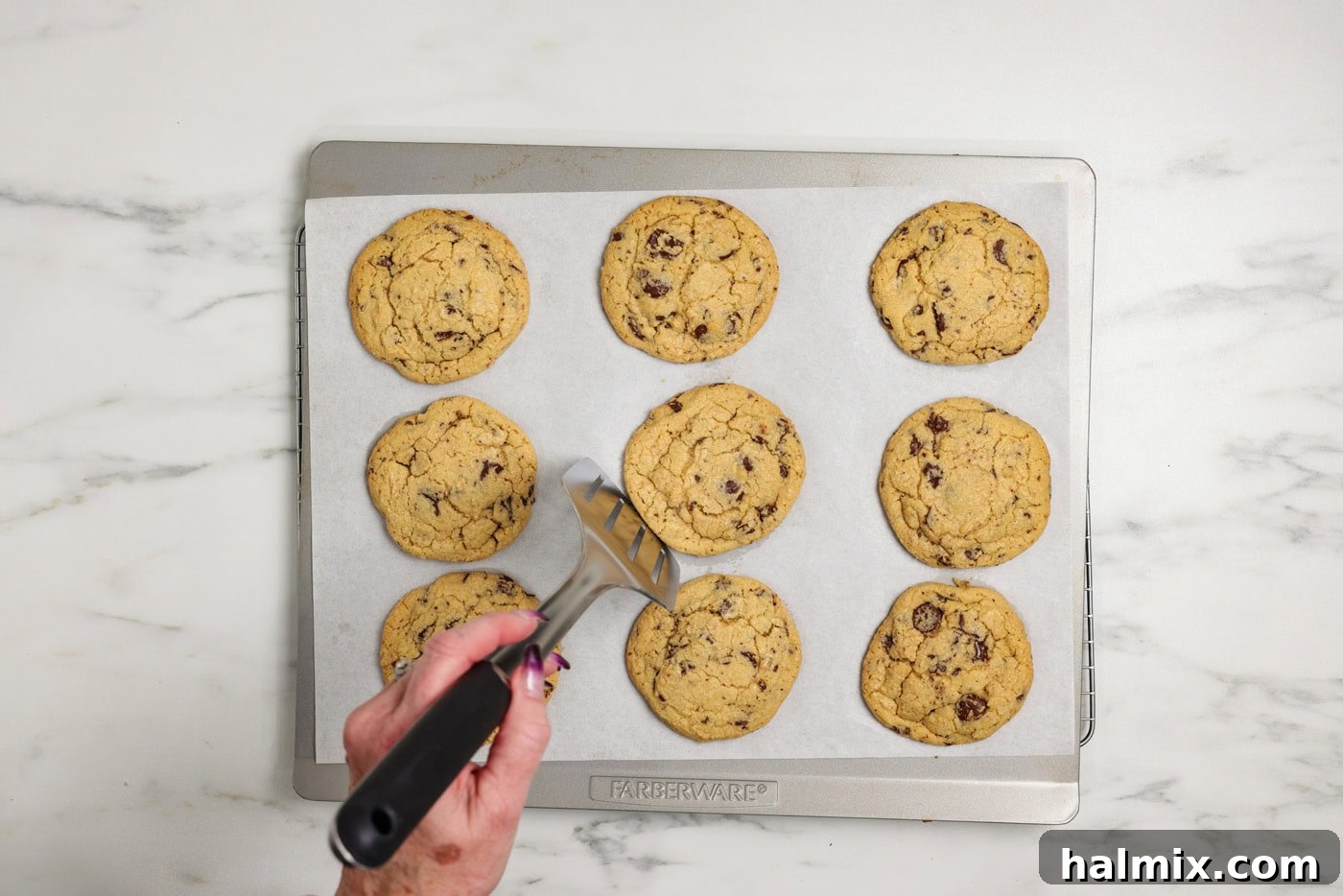 Rounding the edges of freshly baked chocolate chip cookies with a spatula for a perfect shape