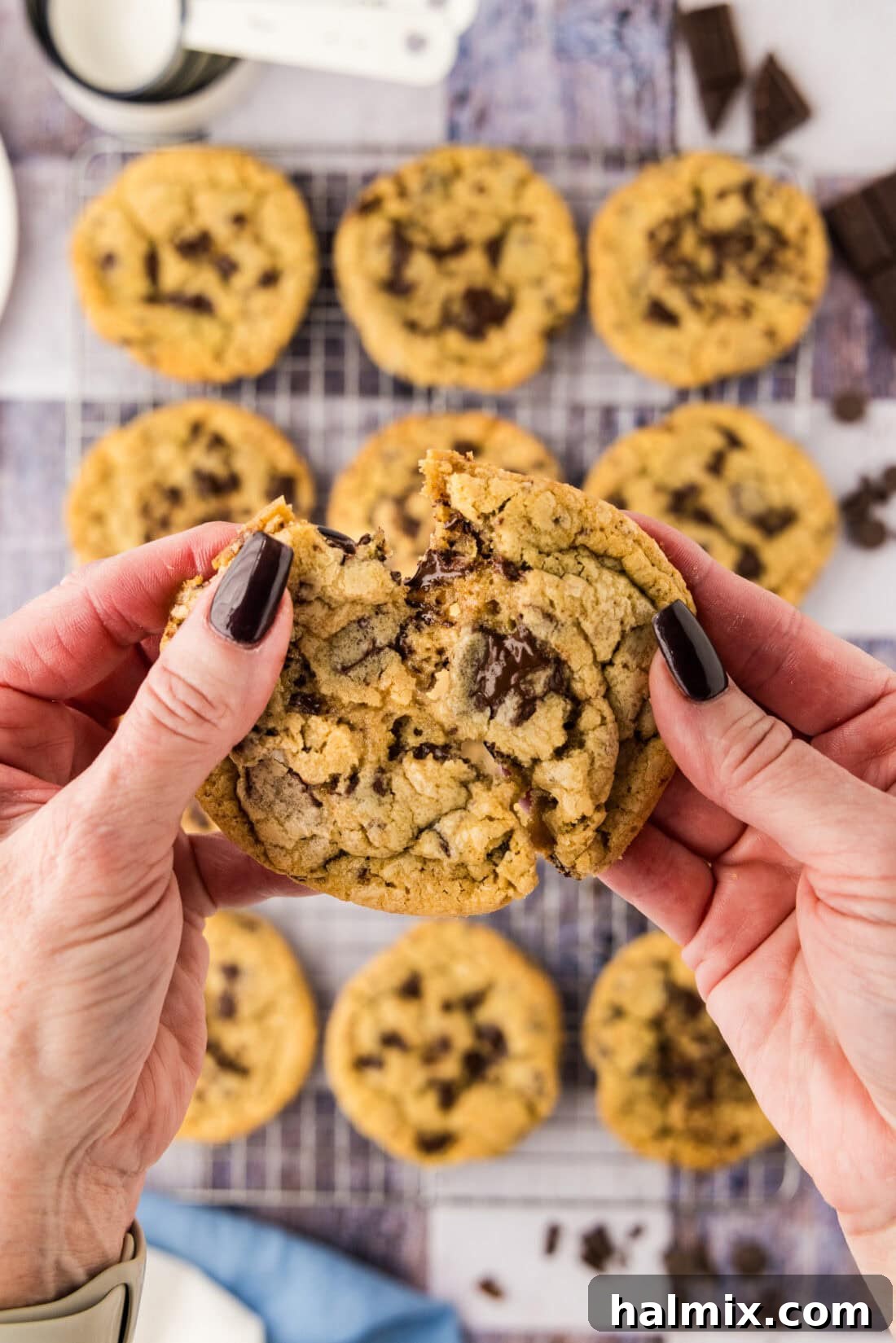 A hand gently breaking apart a warm, gooey jumbo chocolate chip cookie