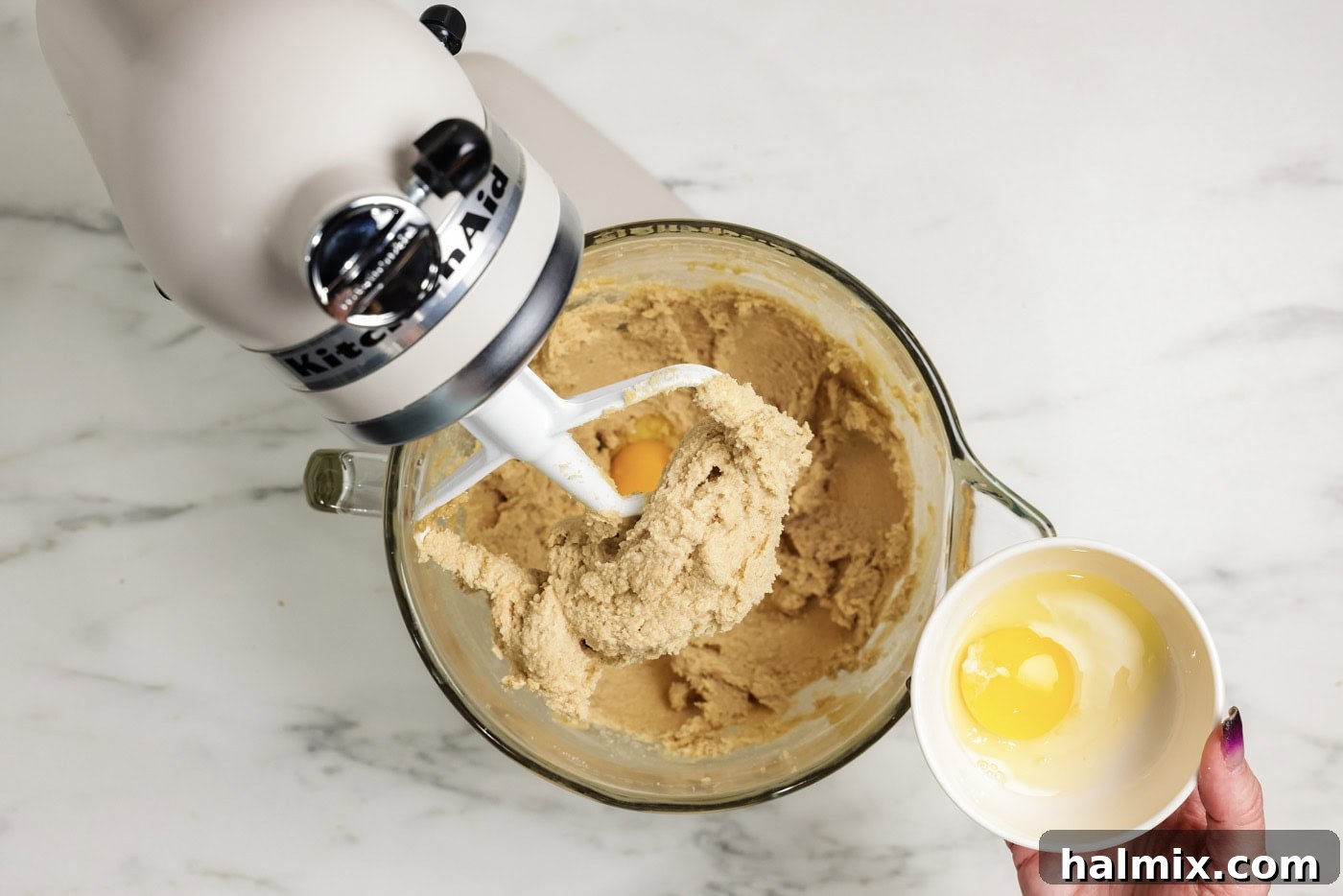 Adding an egg to the creamed butter and sugar mixture in a stand mixer bowl
