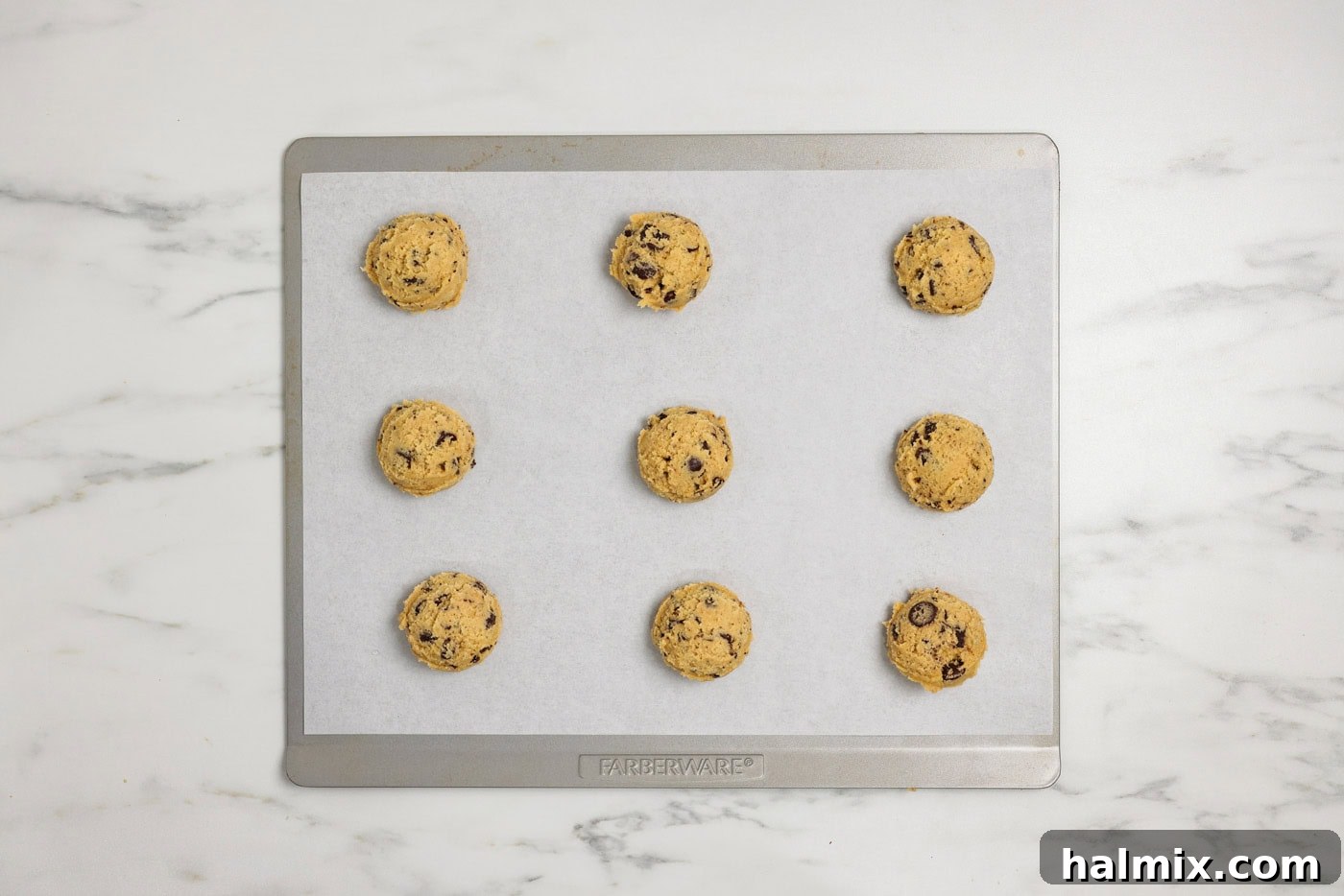 Jumbo chocolate chip cookie dough balls scooped onto a parchment-lined baking sheet