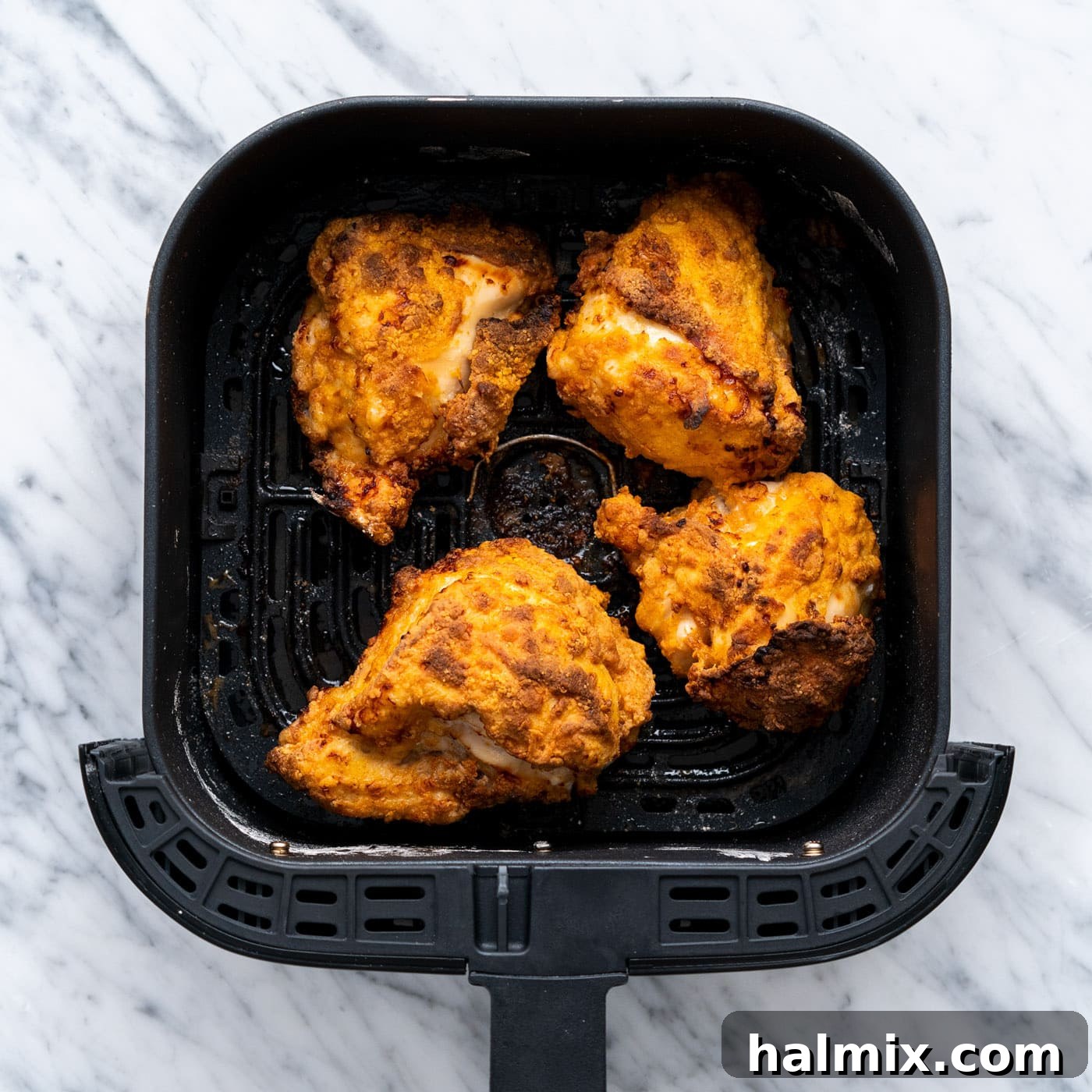 Several pieces of air fryer fried chicken cooking in the air fryer basket, showing a beautiful golden-brown color and crispy texture as they near completion.