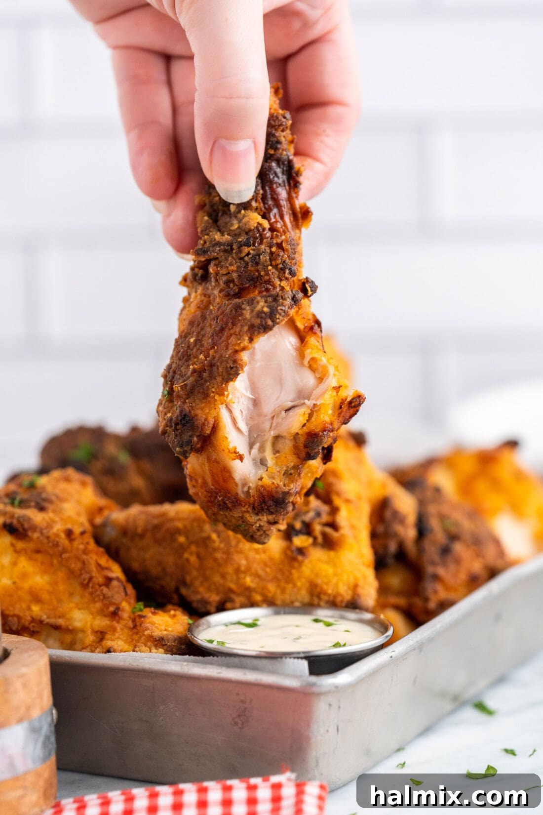 A hand holds a piece of Air Fryer Fried Chicken with a bite taken out, clearly showing the tender, moist chicken inside and the crunchy, seasoned exterior. The focus is on the delicious texture.