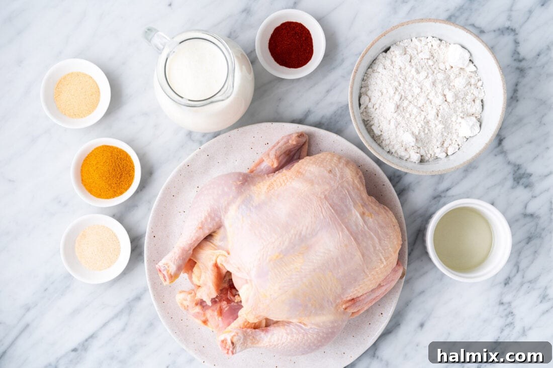 A beautifully arranged flat lay of all the fresh ingredients needed for Air Fryer Fried Chicken, including a whole raw chicken, a bowl of buttermilk, a bowl of flour, and various spice jars.