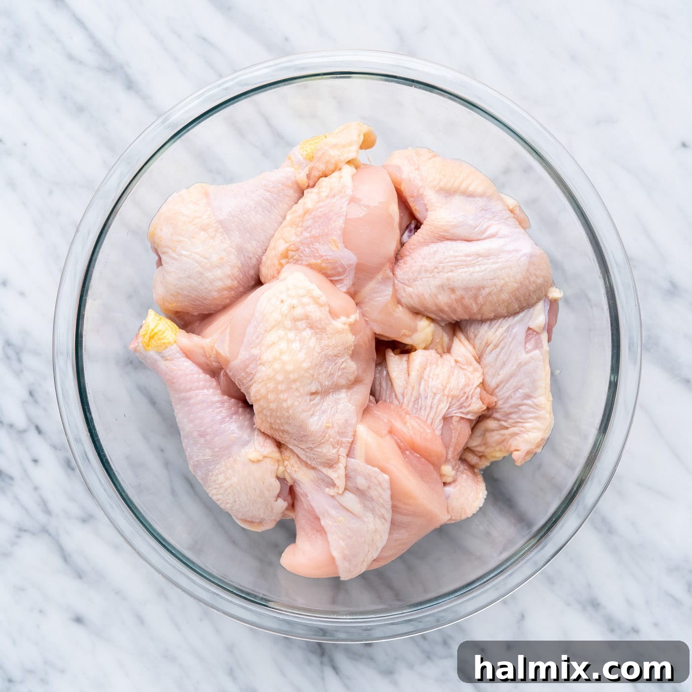 A bowl filled with freshly cut pieces of a whole chicken, ready to be marinated. The pieces include breasts, thighs, legs, and wings, neatly prepared.