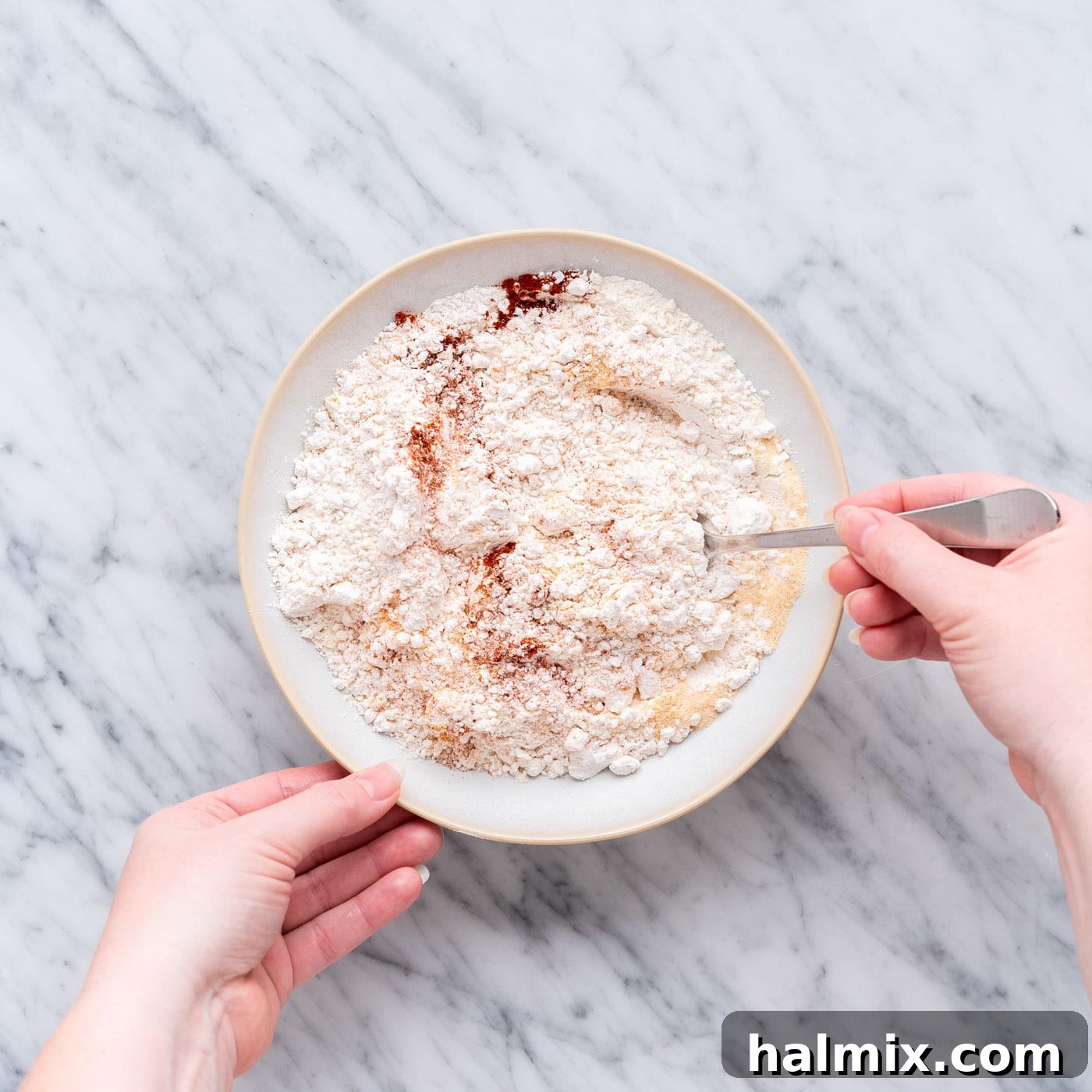 A close-up shot of a shallow bowl where various spices and flour are being mixed together to create the seasoned flour coating for the fried chicken.